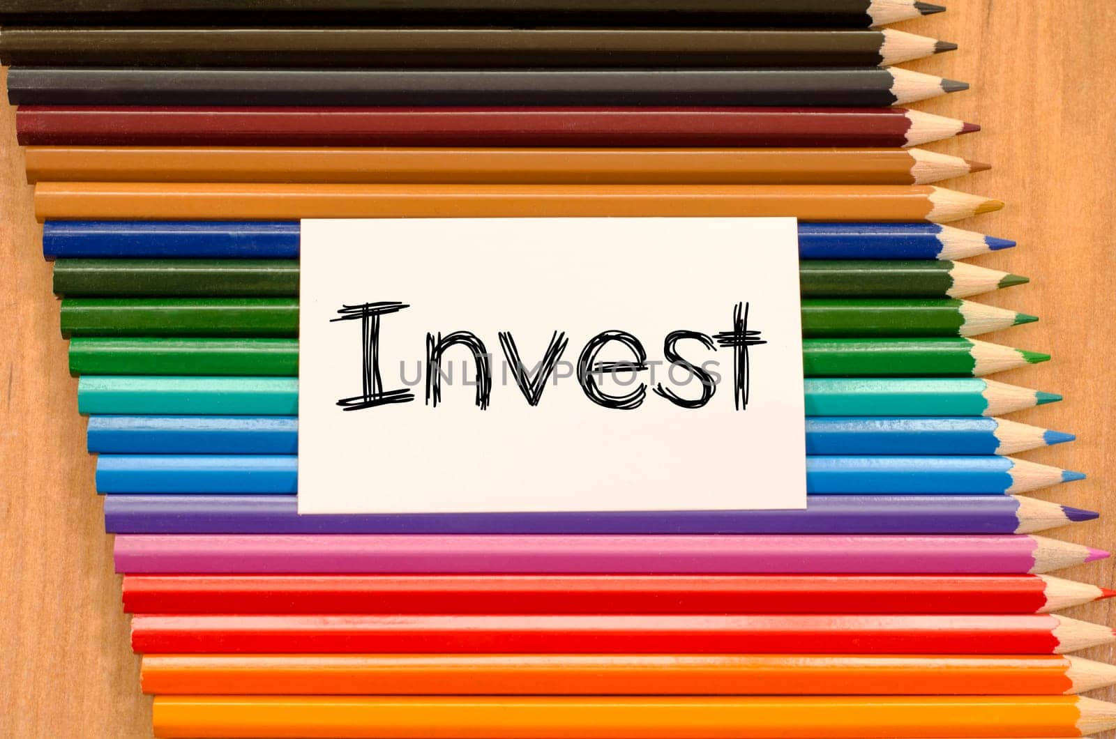 Invest text concept and colored pencil on wooden background