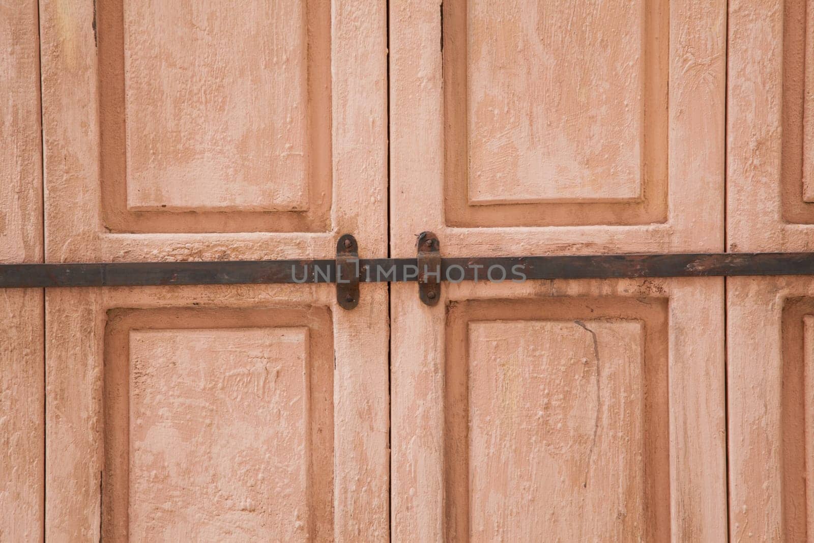 Rose weahtered wood door closed by a rusty rod