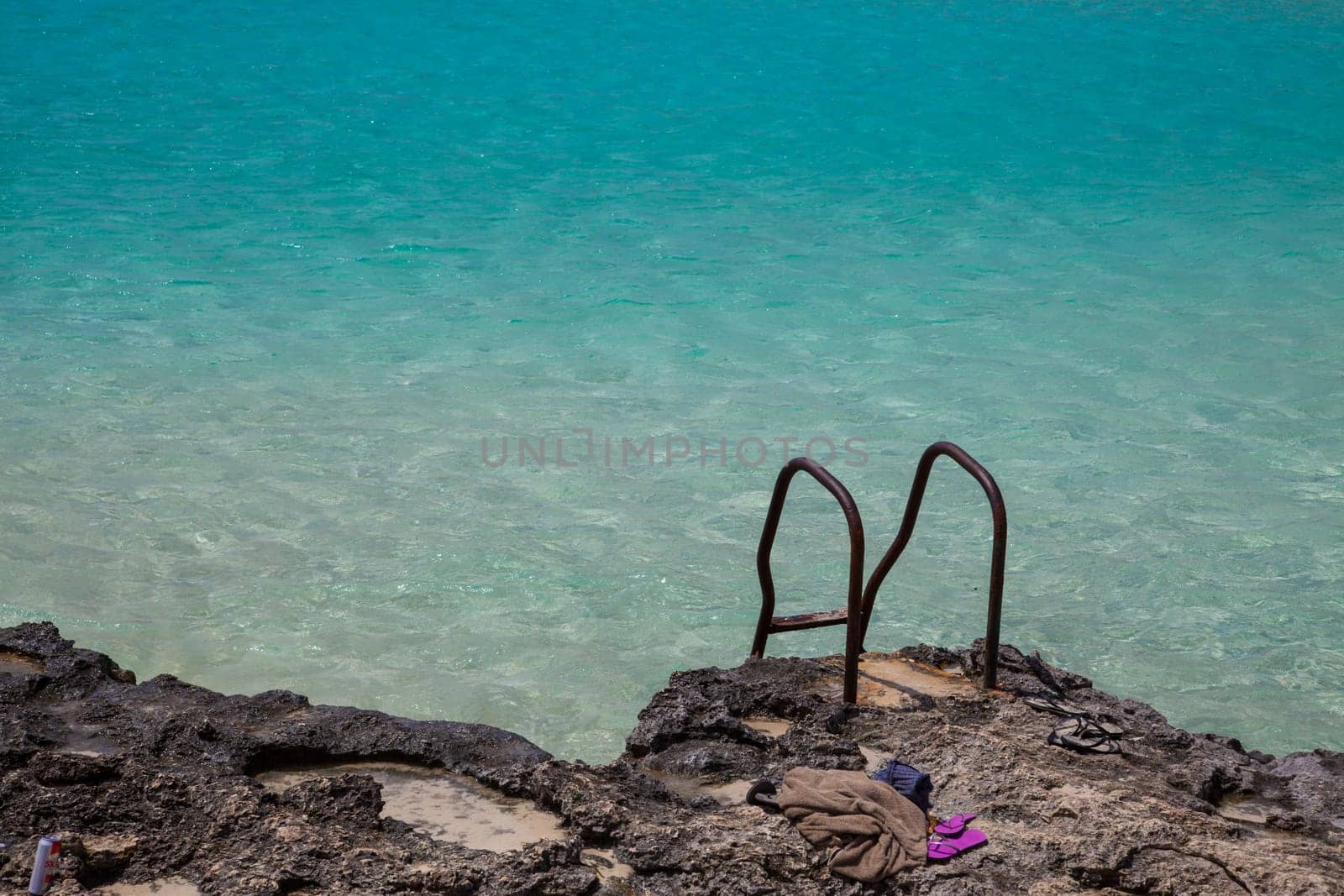 Rusty stairs on rocks to pool-like sea waters with flip-flop