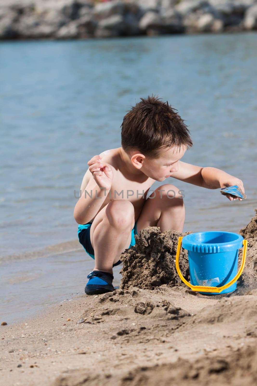 little boy in blue sea playing with mud pies and sand