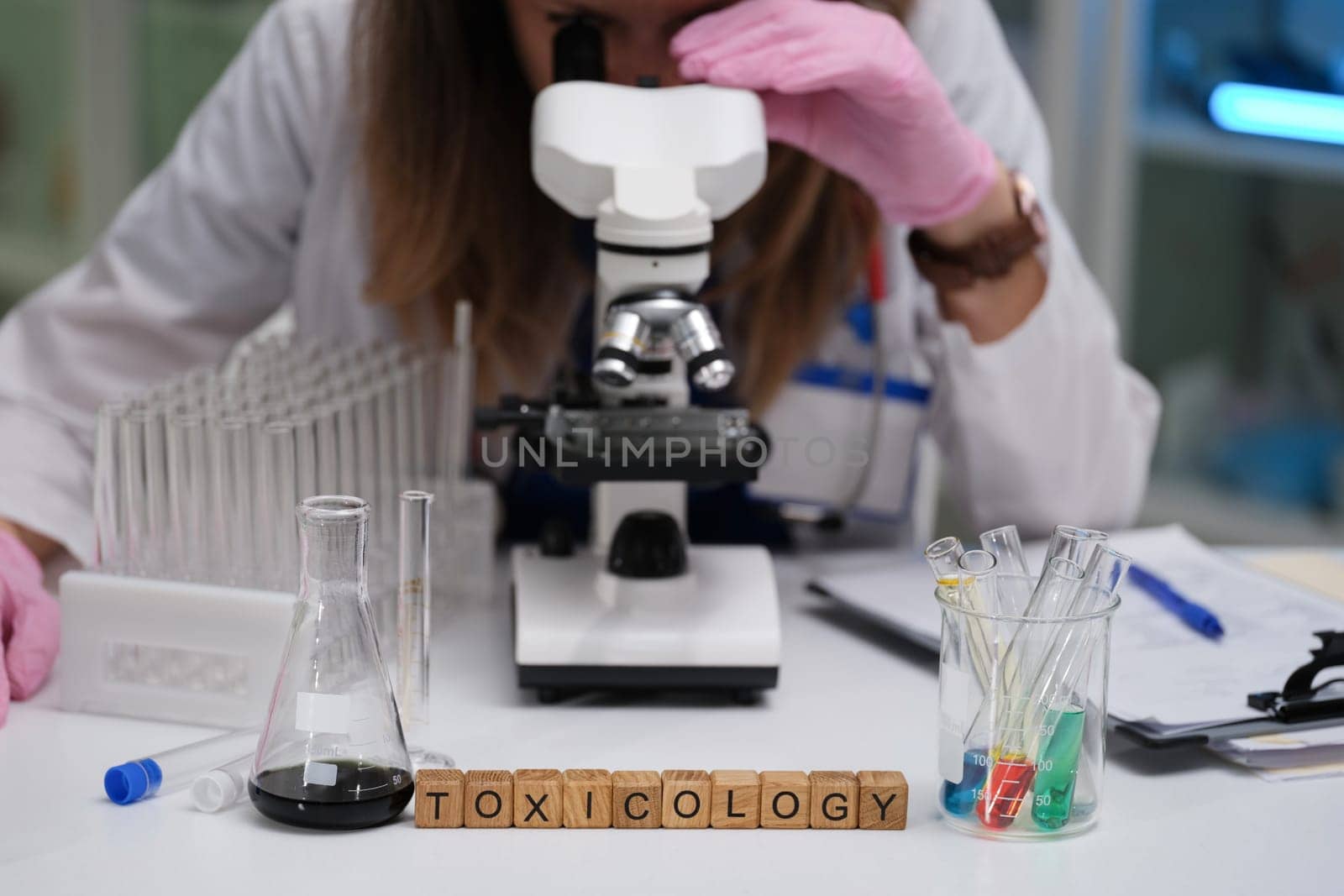 A dedicated scientist is meticulously examining various samples under a microscope in a specialized toxicology lab