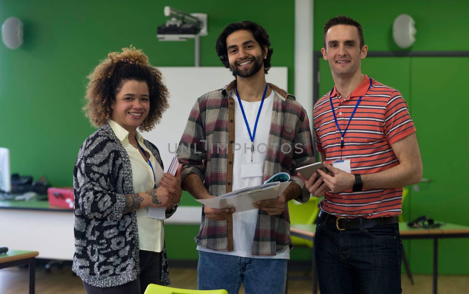 Three teachers standing together with paper work and a digital tablet. They are smiling and looking at the camera.