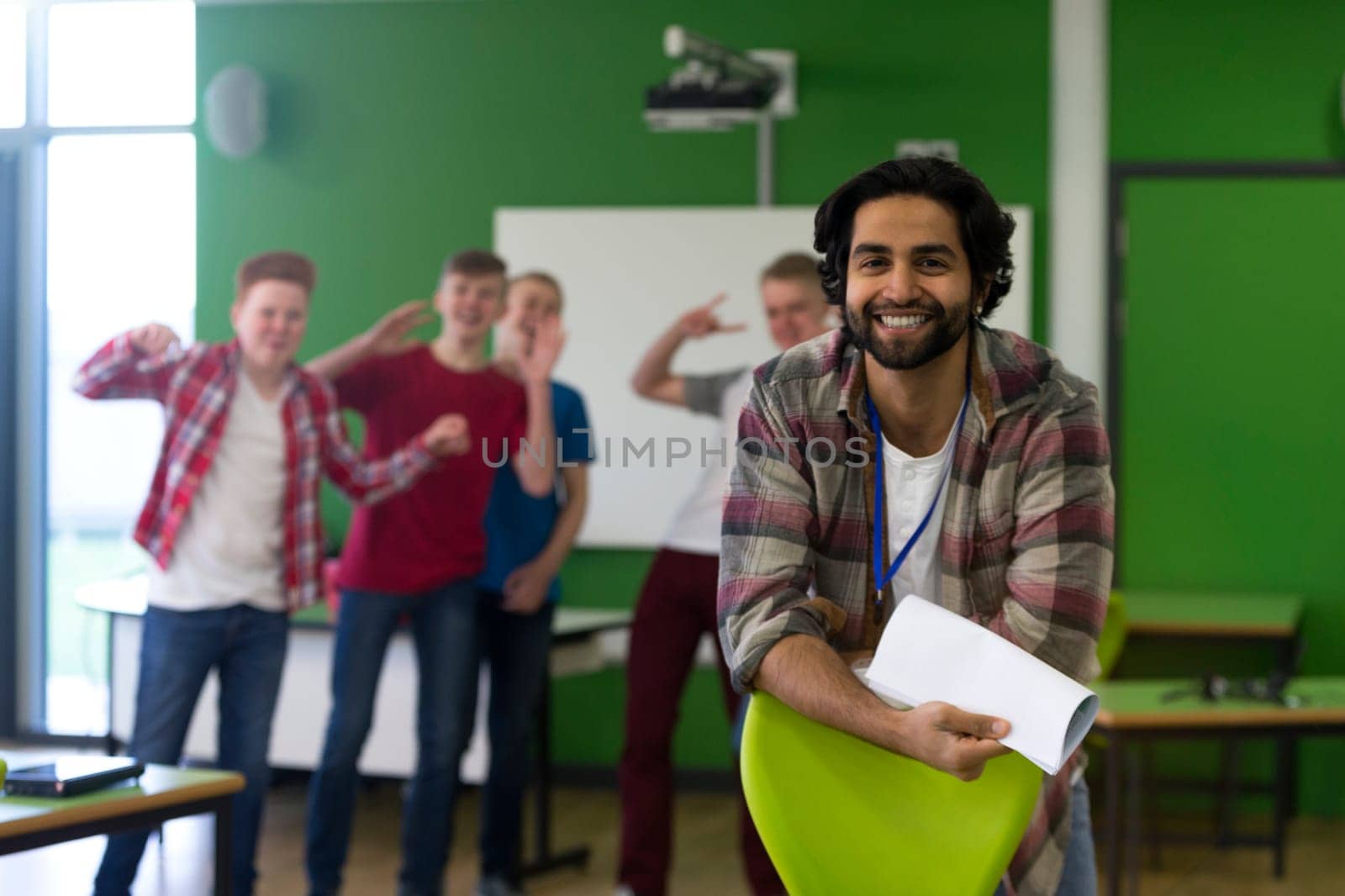 School teacher is smiling for the camera. A group of teenage boys are in the background making sneaky, silly faces at the camera.