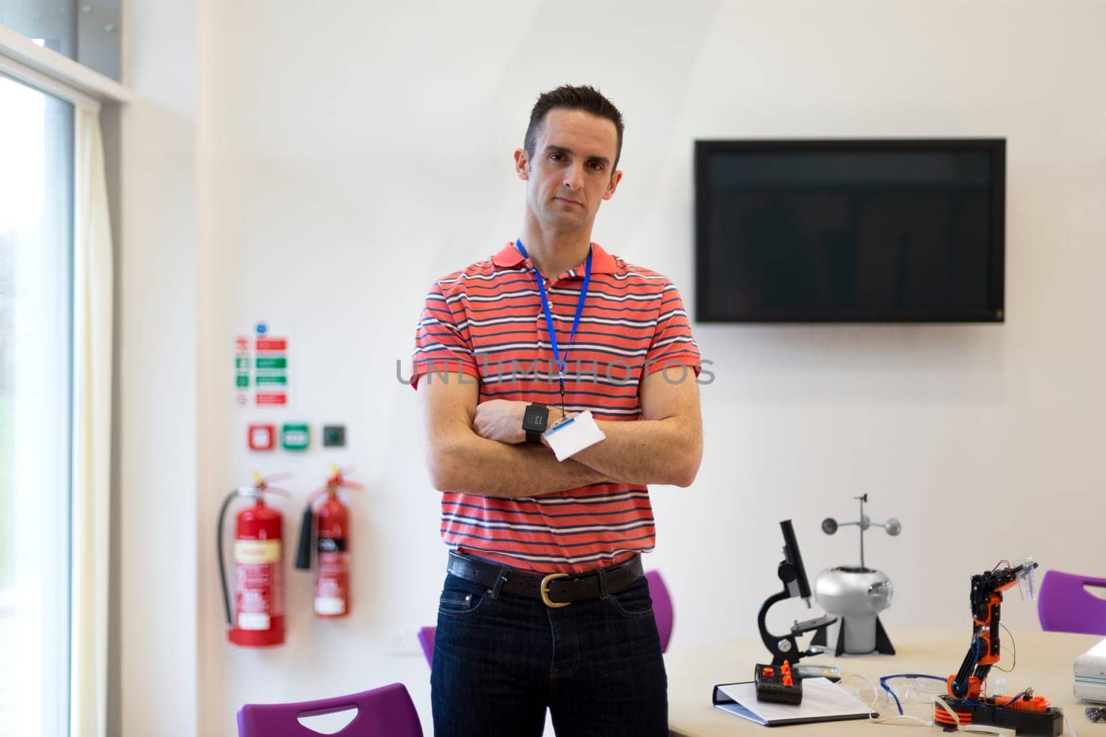 Male teacher standing in a science and technology classroom. He has his arms folded and is looking at the camera.