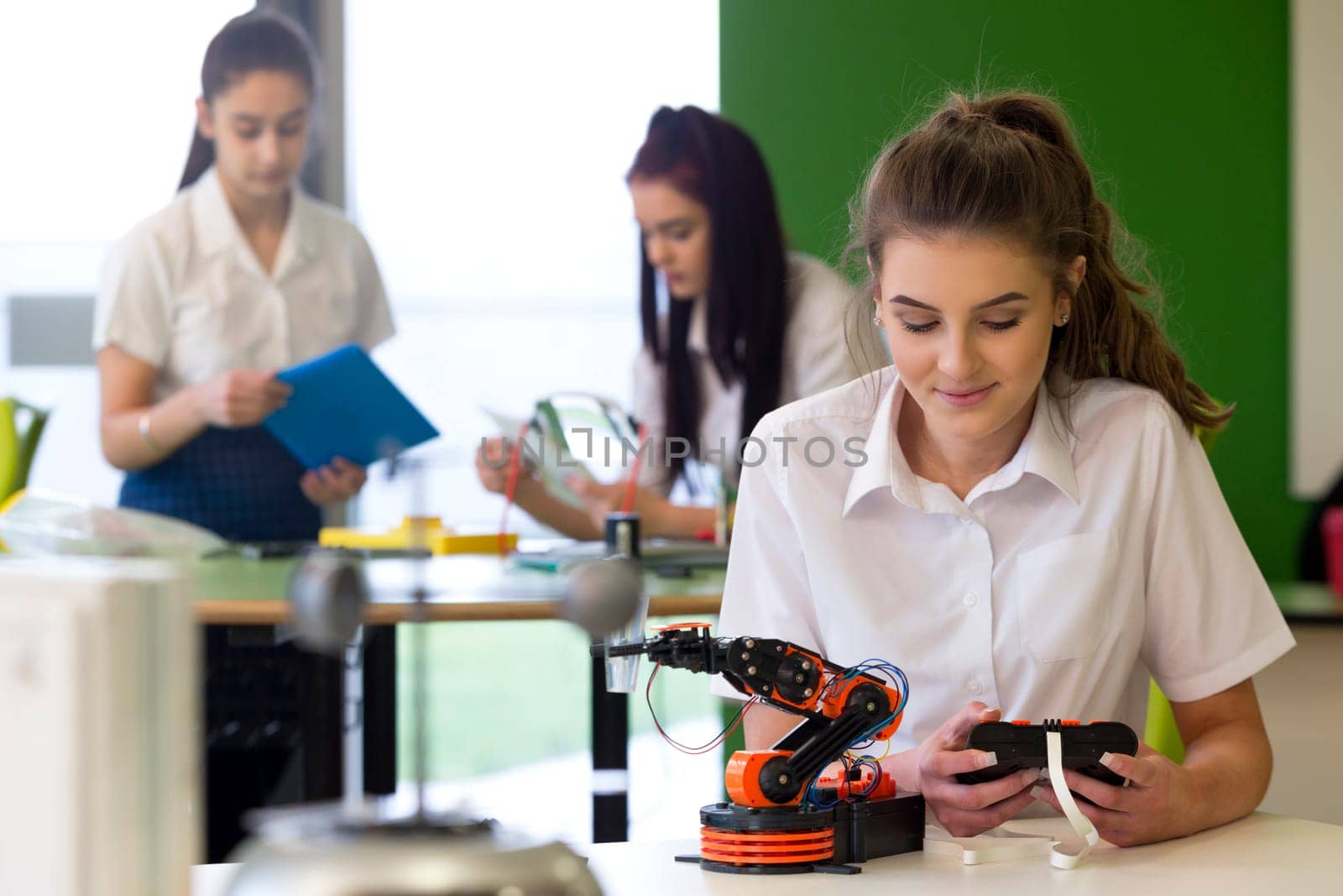 Adolescent girl in a design and technology lesson. She is building a robotic arm and there are other students working in the background.