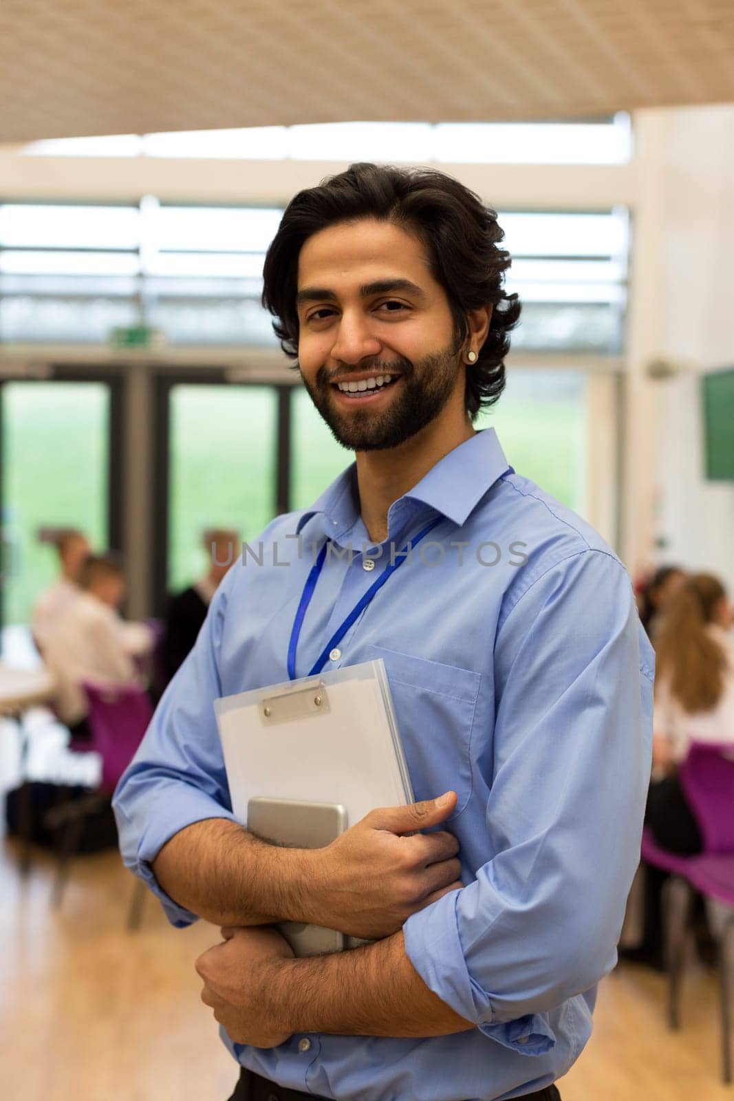 Waist up portrait of a school teacher. He is holding some paperwork and a digital tablet.