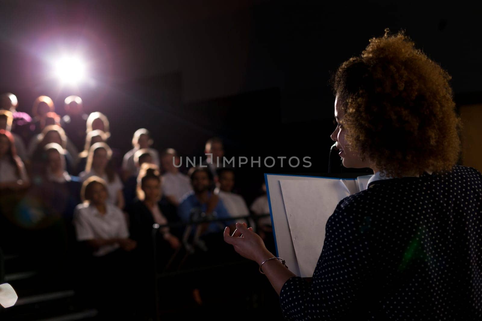 Female teacher giving a speech in a lecture hall to students and teachers.