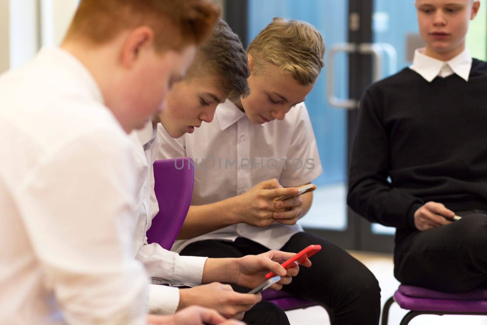 Group of male high school students on their break at school. They are all looking at smartphones.