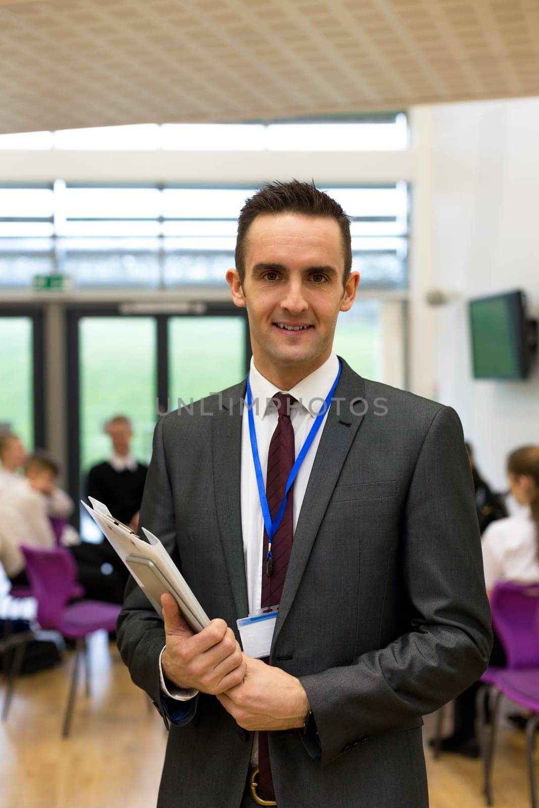 Waist up portrait of a school teacher. He is holding some paperwork and a digital tablet.
