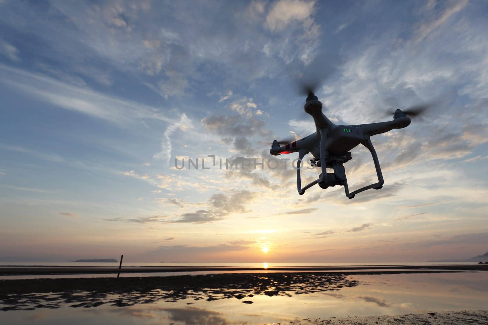 KAGAWA, JAPAN - JUNE 10, 2016: Remote controlled drone Dji Phantom 3 equipped with high resolution video camera flying above the beach against a sunset.