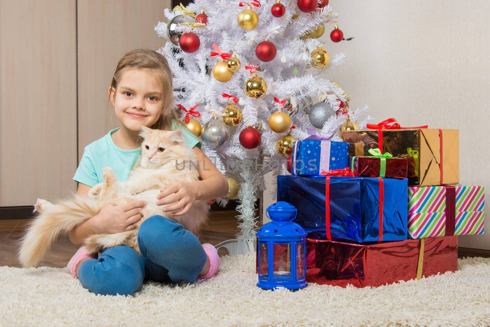 Joyful seven year old girl with a cat sitting under the Christmas tree with gifts
