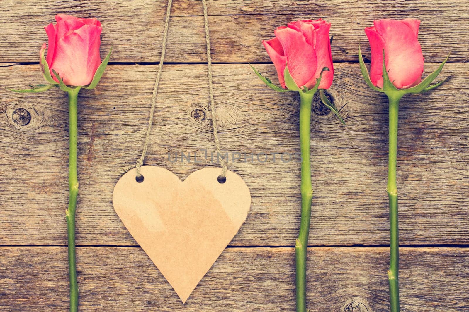Blank heart shaped tag and roses on wooden background.