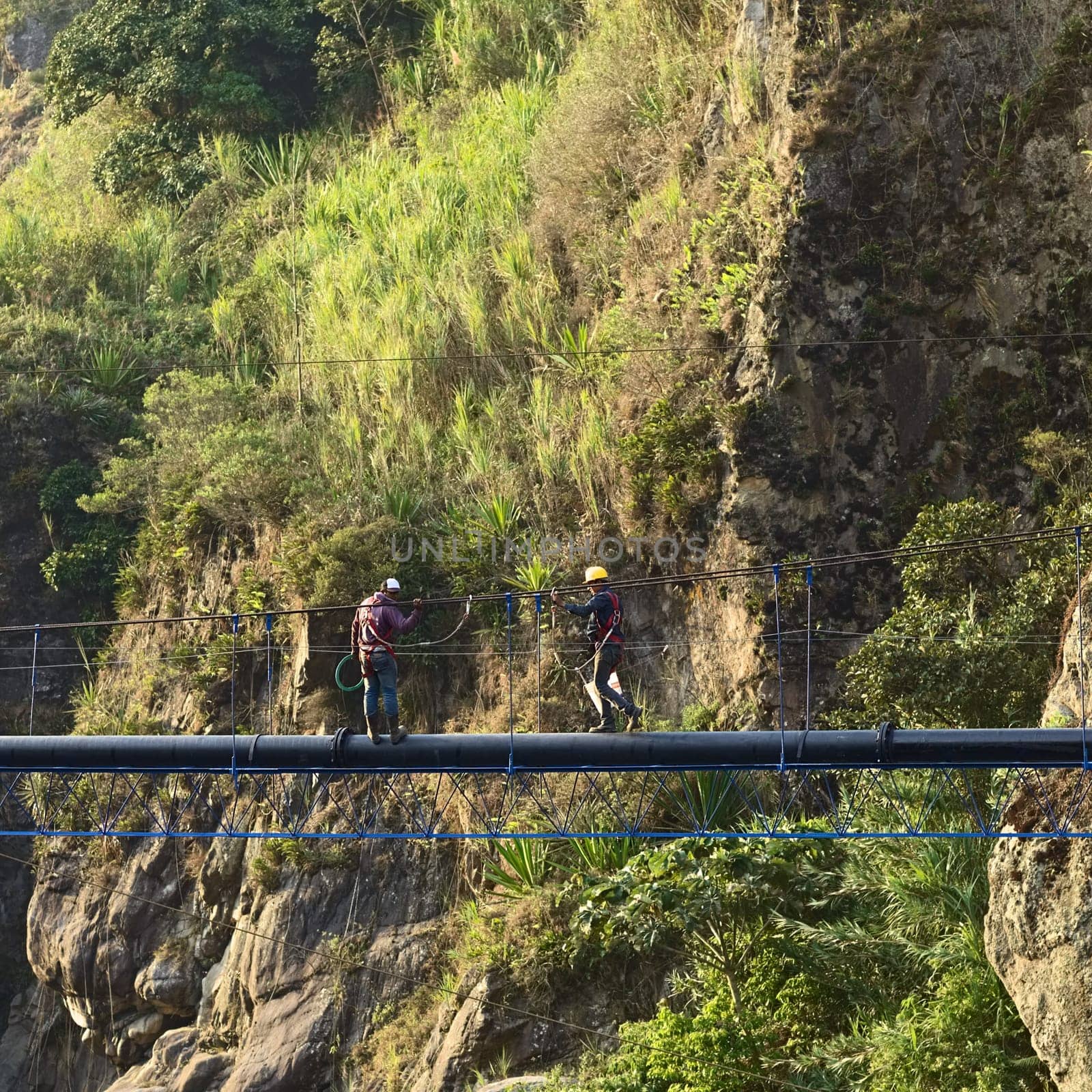 BANOS, ECUADOR - FEBRUARY 18, 2014: Unidentified young men working on a pipe over the canyon of the river Pastaza on February 18, 2014 at Banos, Ecuador.