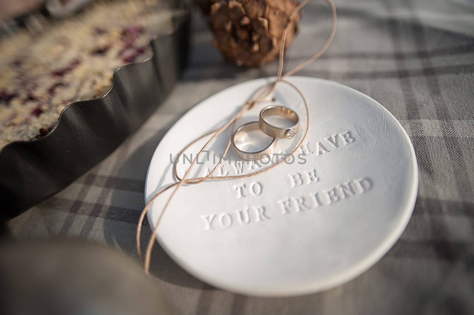 Wedding rings in white gold, white clay saucer with the word always have to be your friend