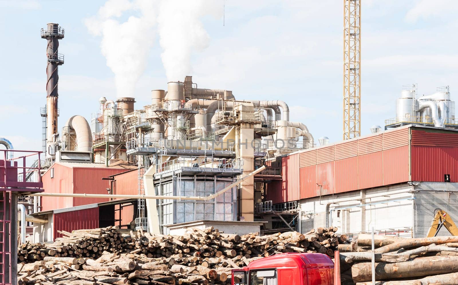 industrial plant of a furniture factory with smoking smokestacks,tubes,silos,crane ,truck and trunks.