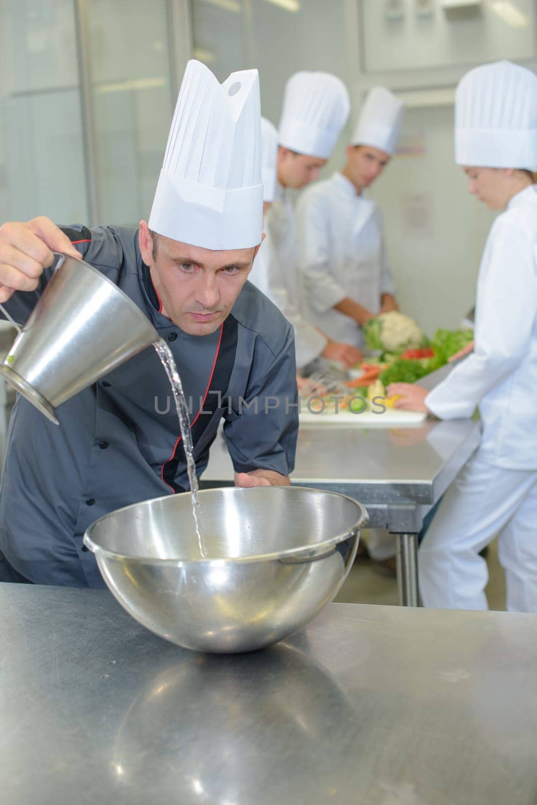 Chef pouring liquid into stainless steel bowl