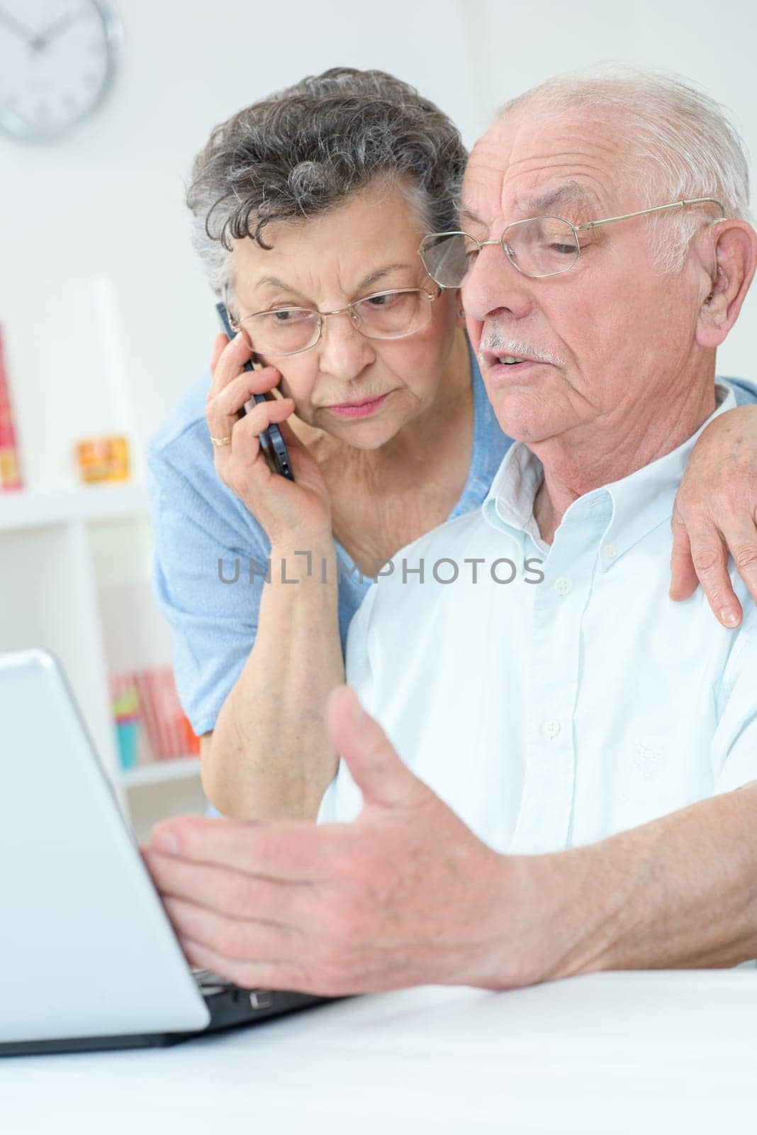 Elderly couple using laptop, wife on telephone