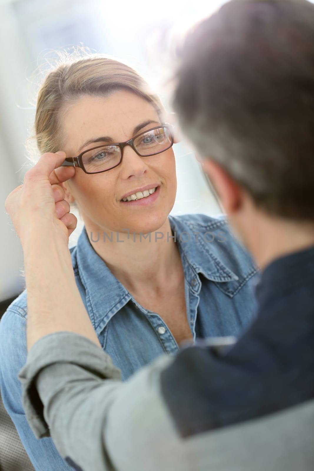 Mature blond woman with optician trying eyeglasses