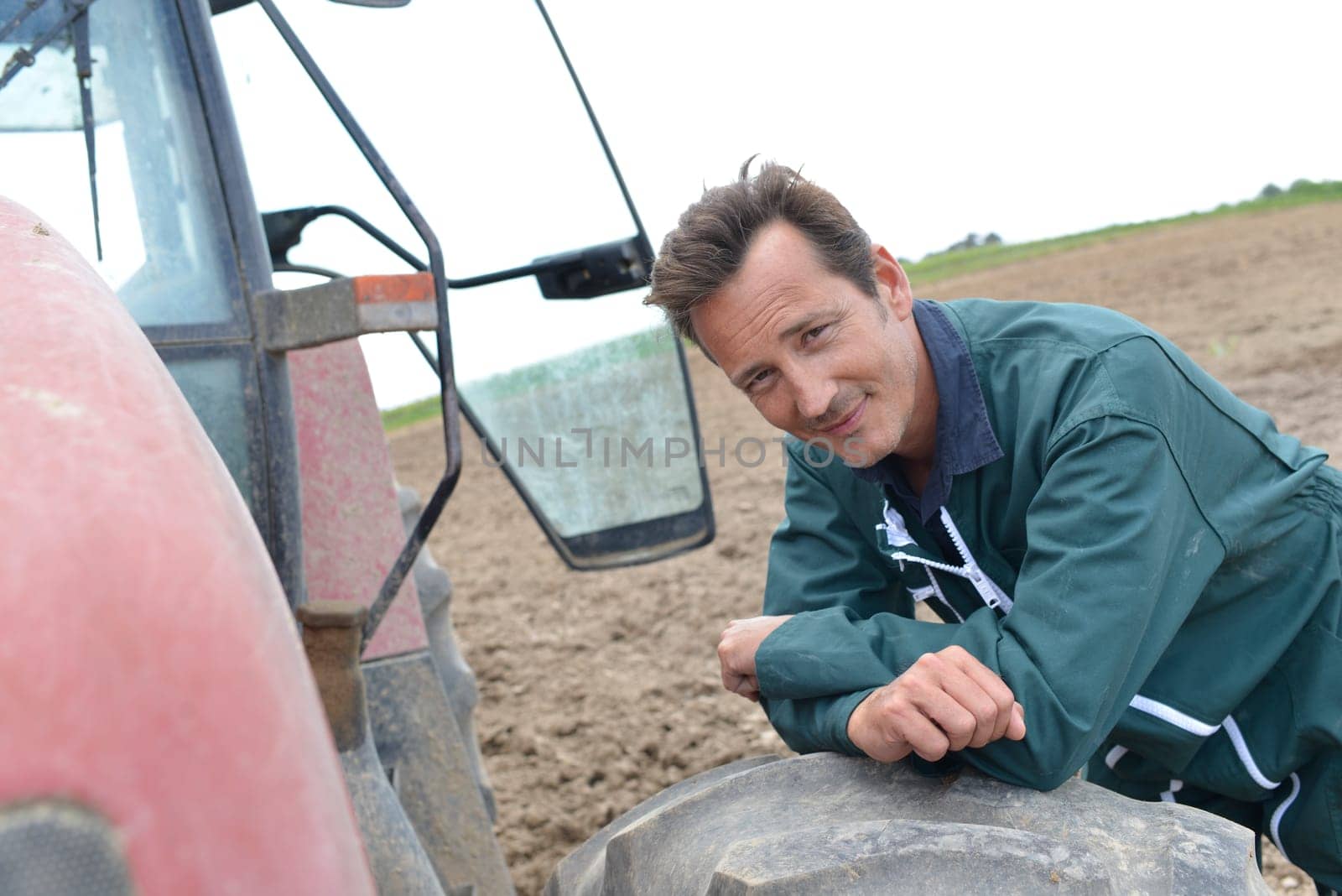 Smiling handsome farmer leaning on tractor