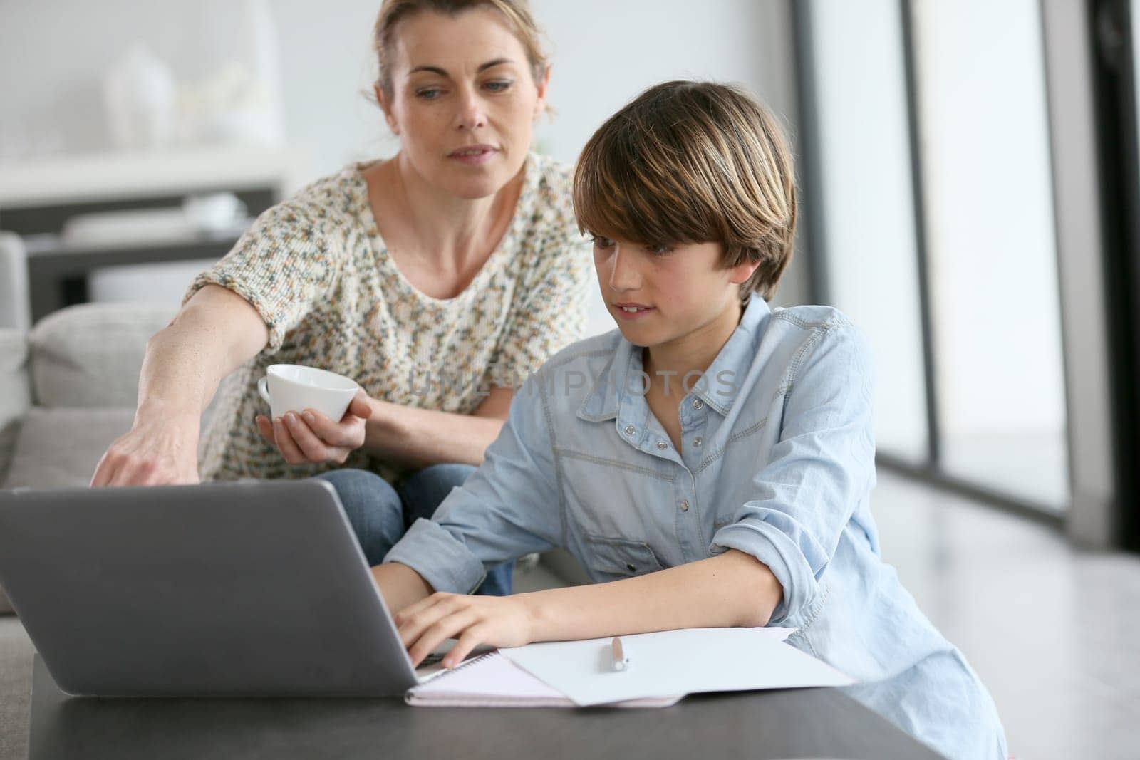 Mother looking after son doing homework on laptop