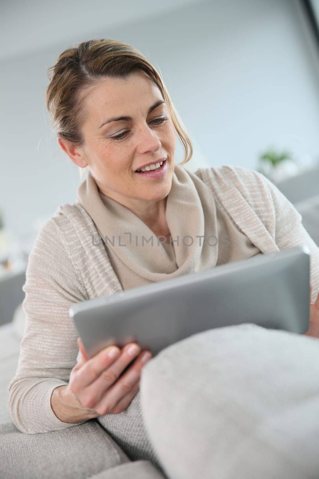 Mature woman sitting in sofa and websurfing with tablet