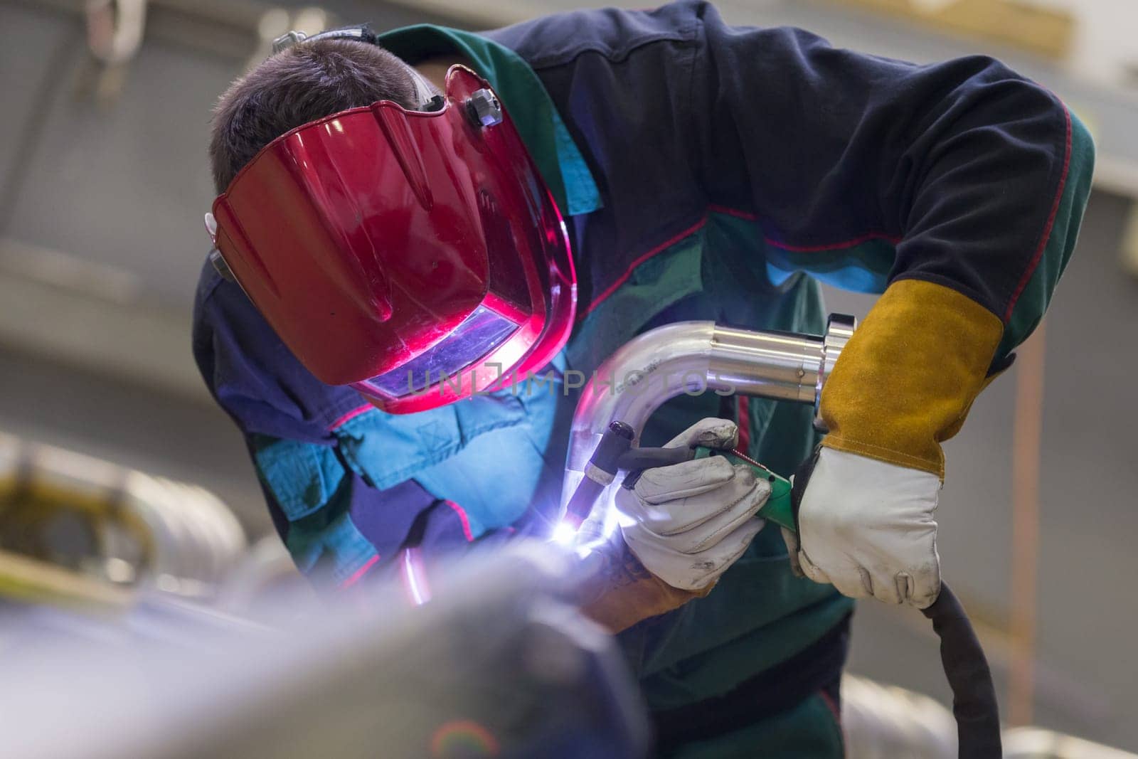 Industrial worker with protective mask welding inox elements in steel structures manufacture workshop.