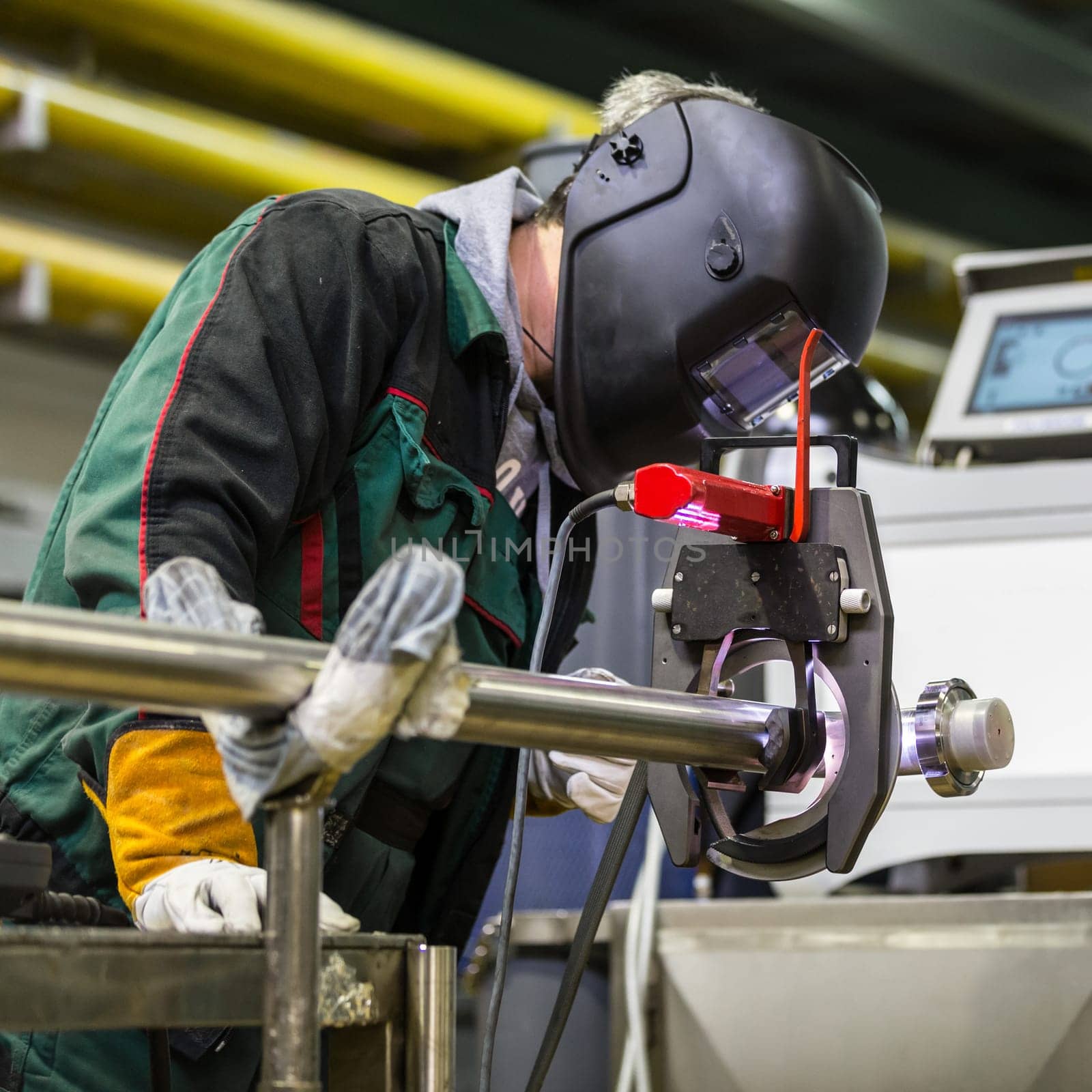 Industrial operator setting  computer controlled process of orbital welding machine in inox pipes manufacturing workshop.
