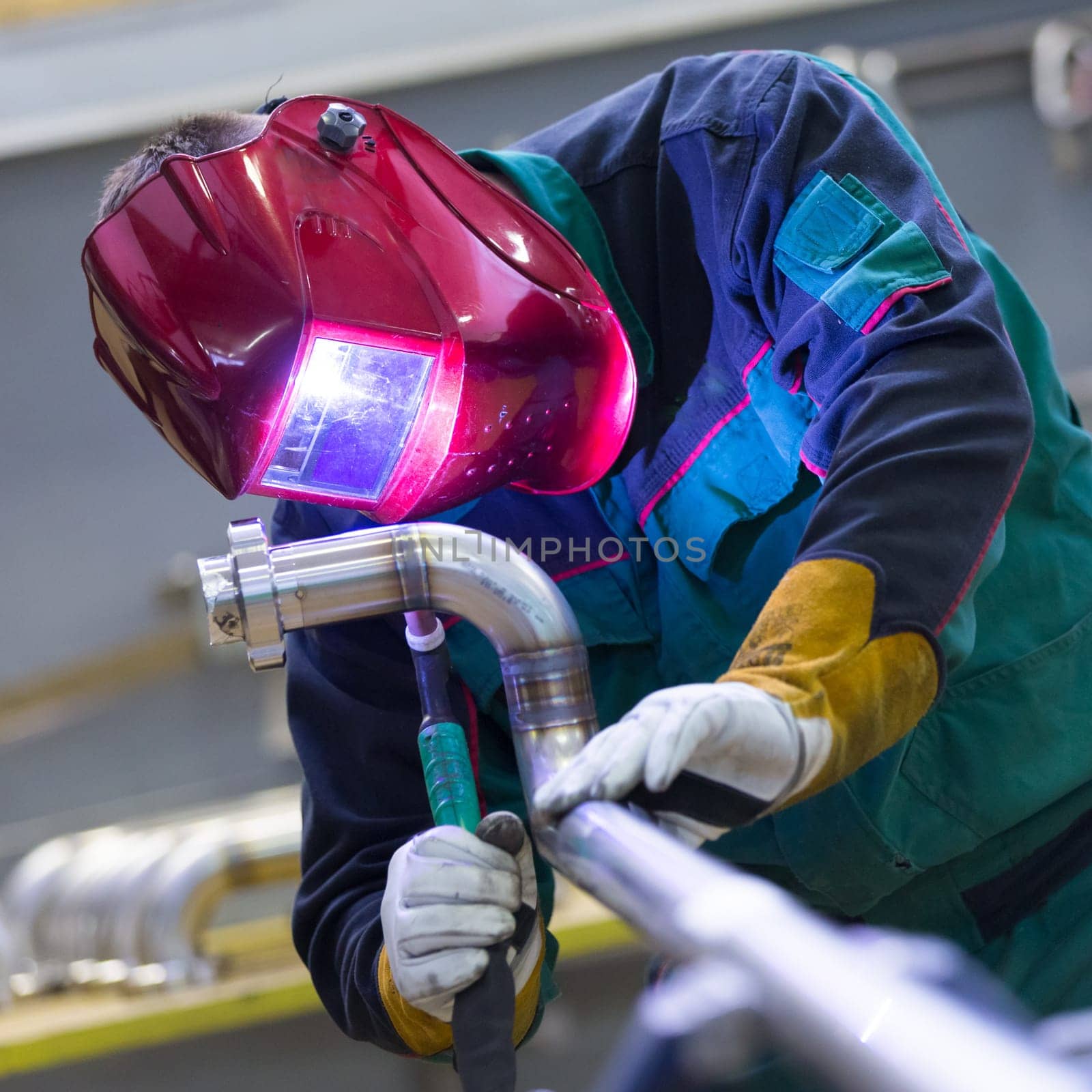 Industrial worker with protective mask welding inox elements in steel structures manufacture workshop.