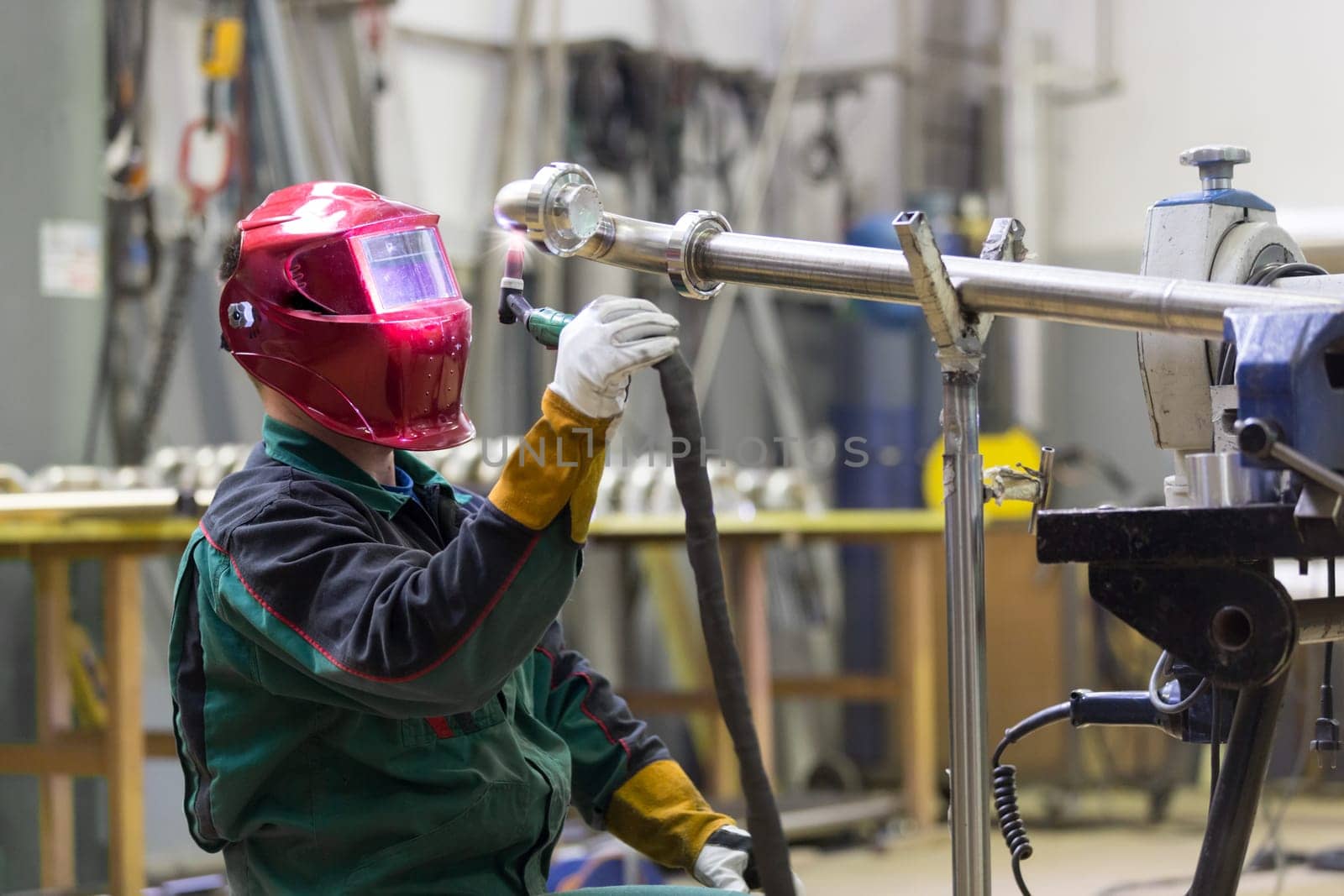 Industrial worker with protective mask welding inox elements in steel structures manufacture workshop.