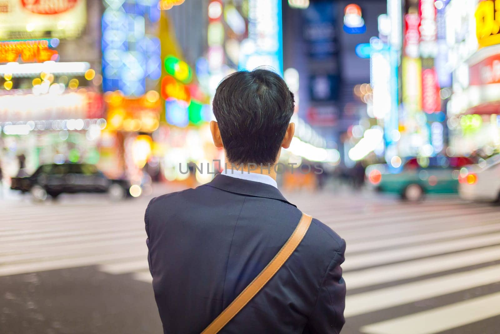 Solitary japanese corporative businessman in suit, after work, waiting on crossroad in Kabukicho, entertainment and red-light district in Shinjuku, Tokyo, Japan.