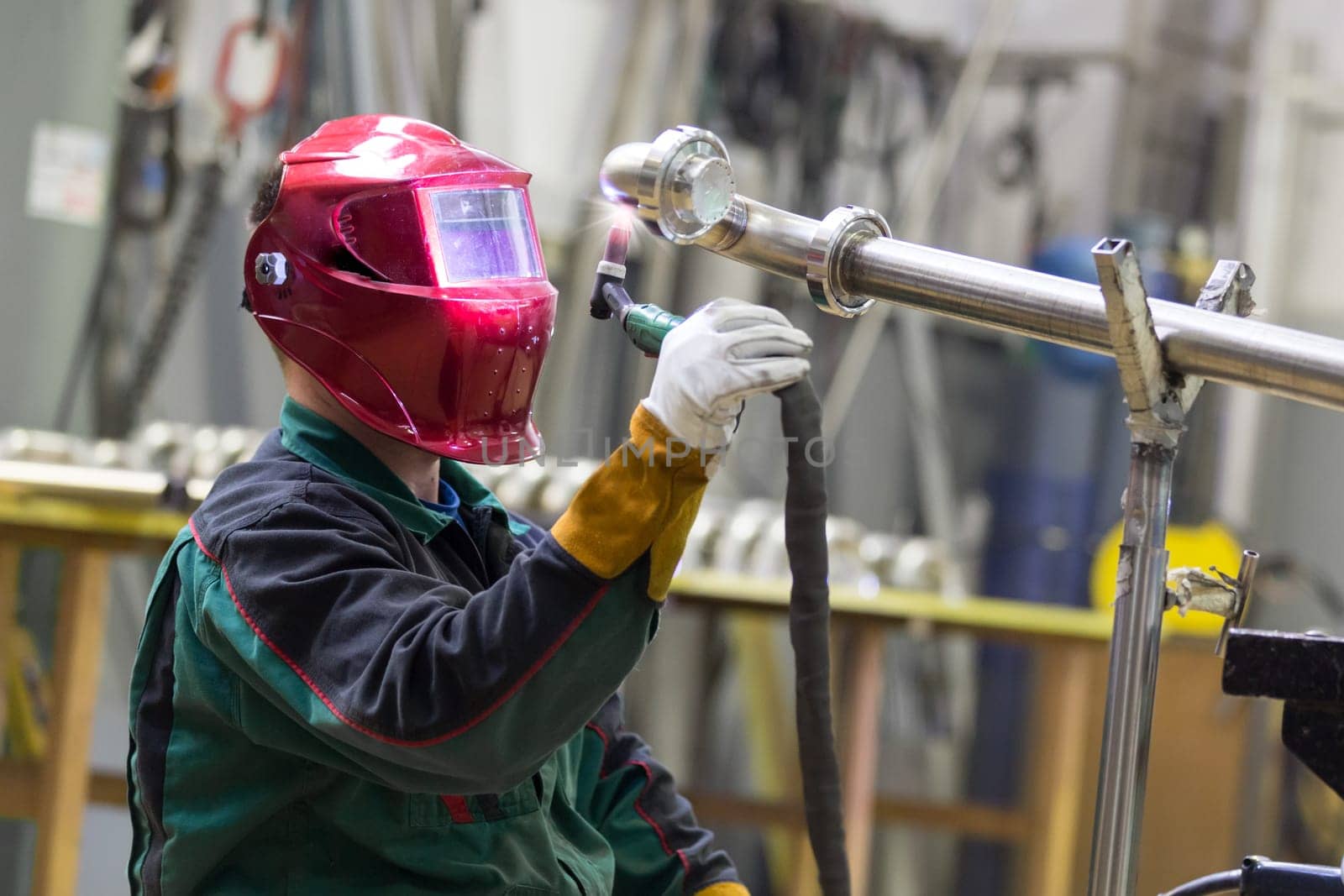 Industrial worker with protective mask welding inox elements in steel structures manufacture workshop.