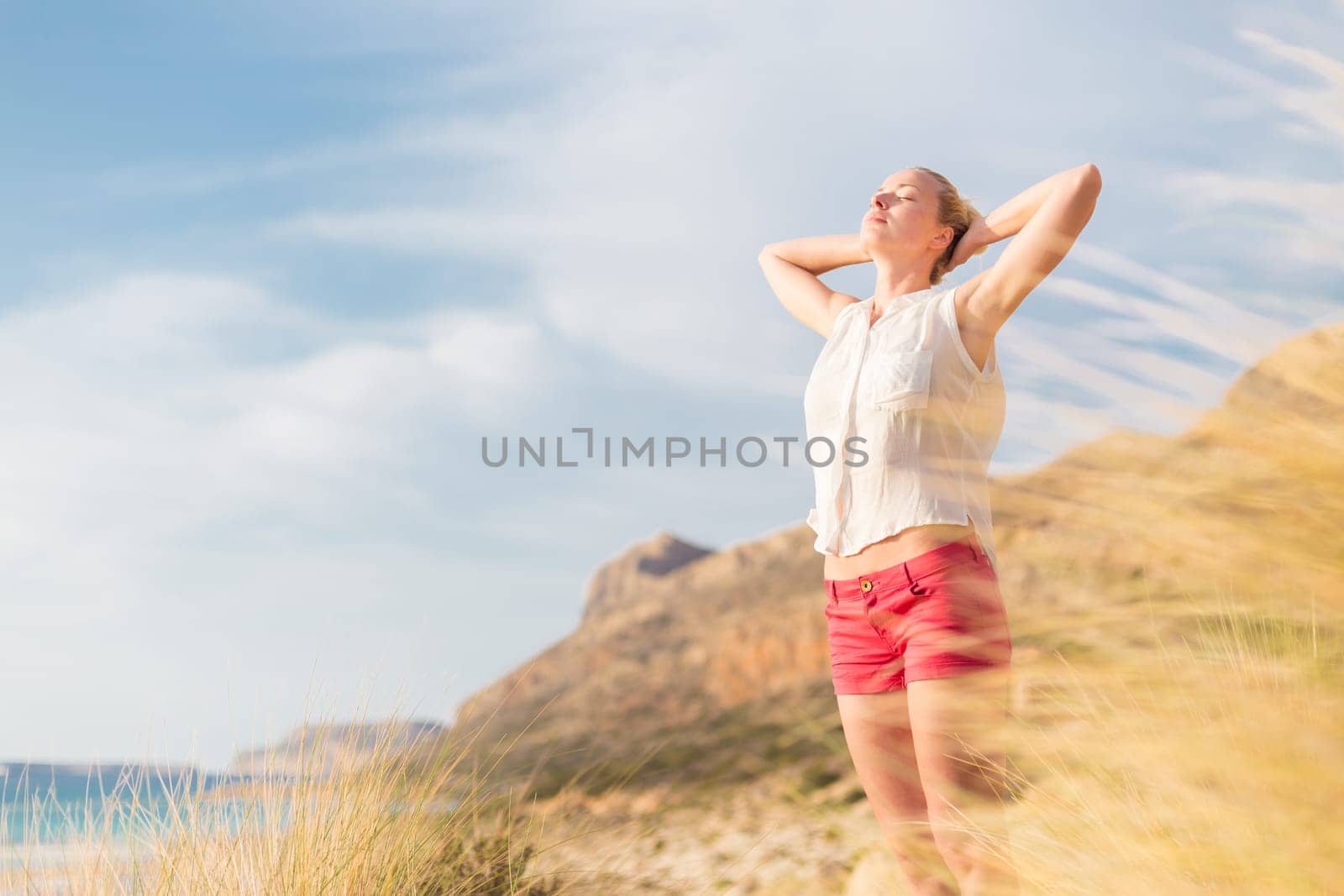 Relaxed woman, arms rised, enjoying sun, freedom and life an a beautiful beach. Young lady feeling free, relaxed and happy. Concept of vacations, freedom, happiness, enjoyment and well being.
