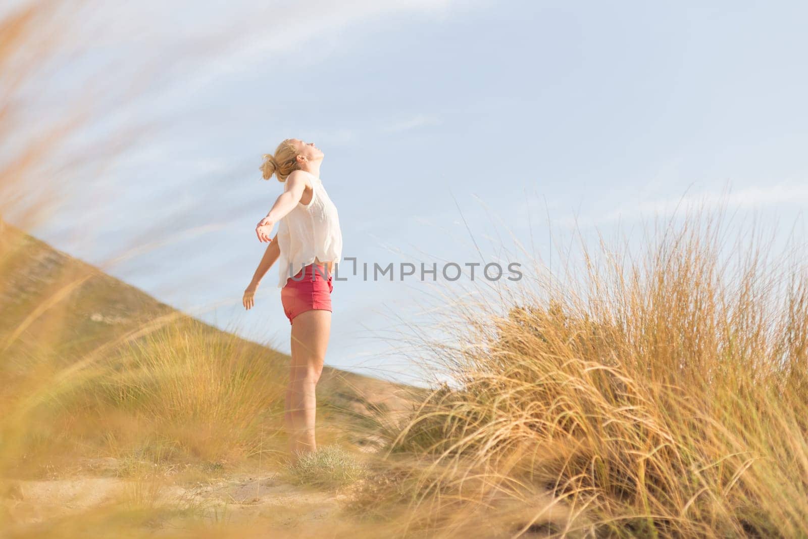 Relaxed woman, arms rised, enjoying sun, freedom and life an a beautiful beach. Young lady feeling free, relaxed and happy. Concept of vacations, freedom, happiness, enjoyment and well being.
