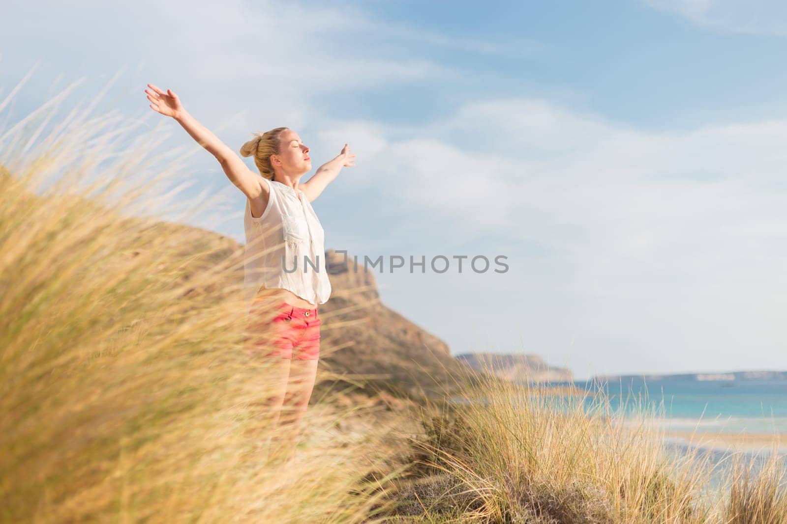 Relaxed woman, arms rised, enjoying sun, freedom and life an a beautiful beach. Young lady feeling free, relaxed and happy. Concept of vacations, freedom, happiness, enjoyment and well being.