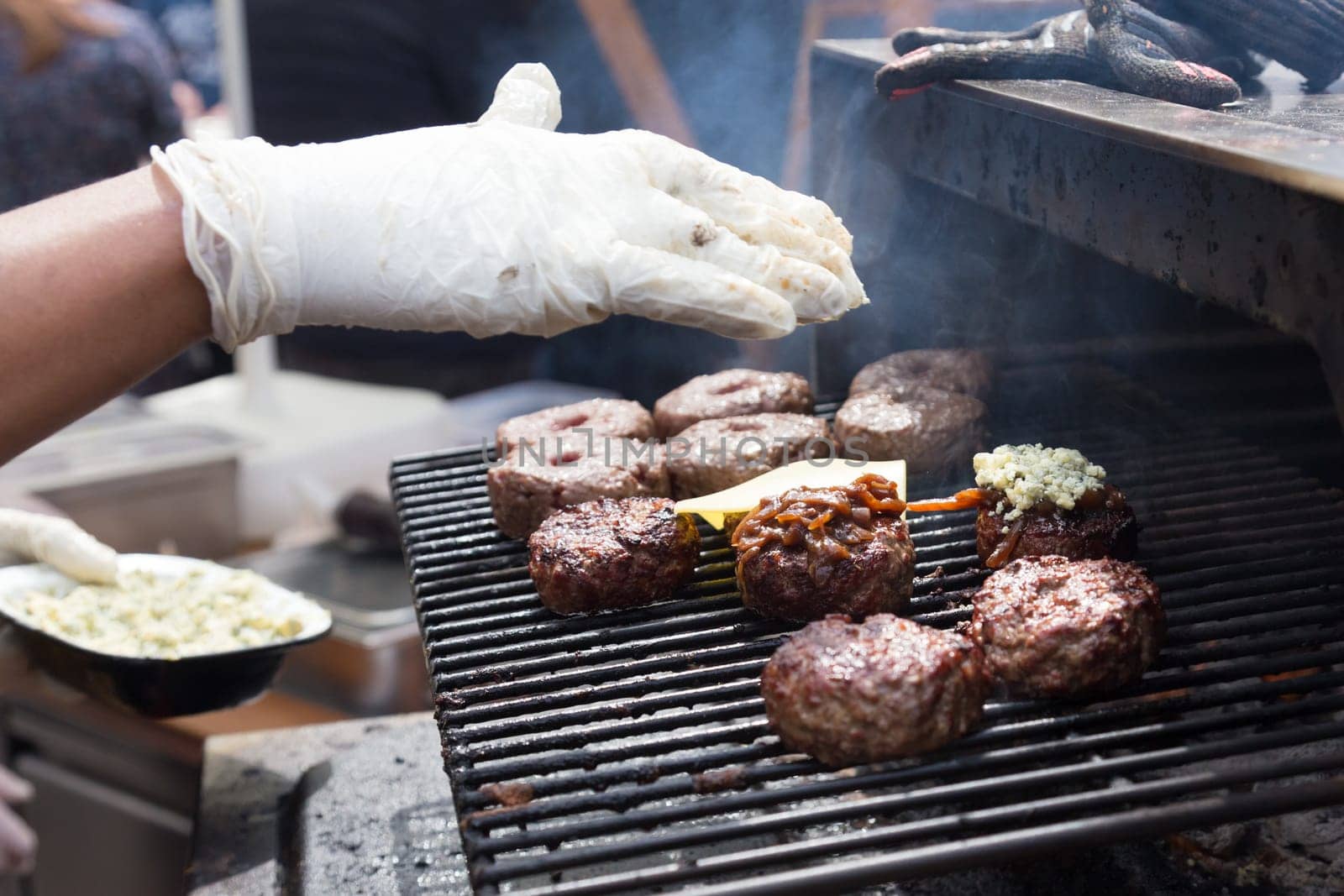 Chef making beef burgers outdoor on open kitchen international food festival event. Street food ready to serve on a food stall.