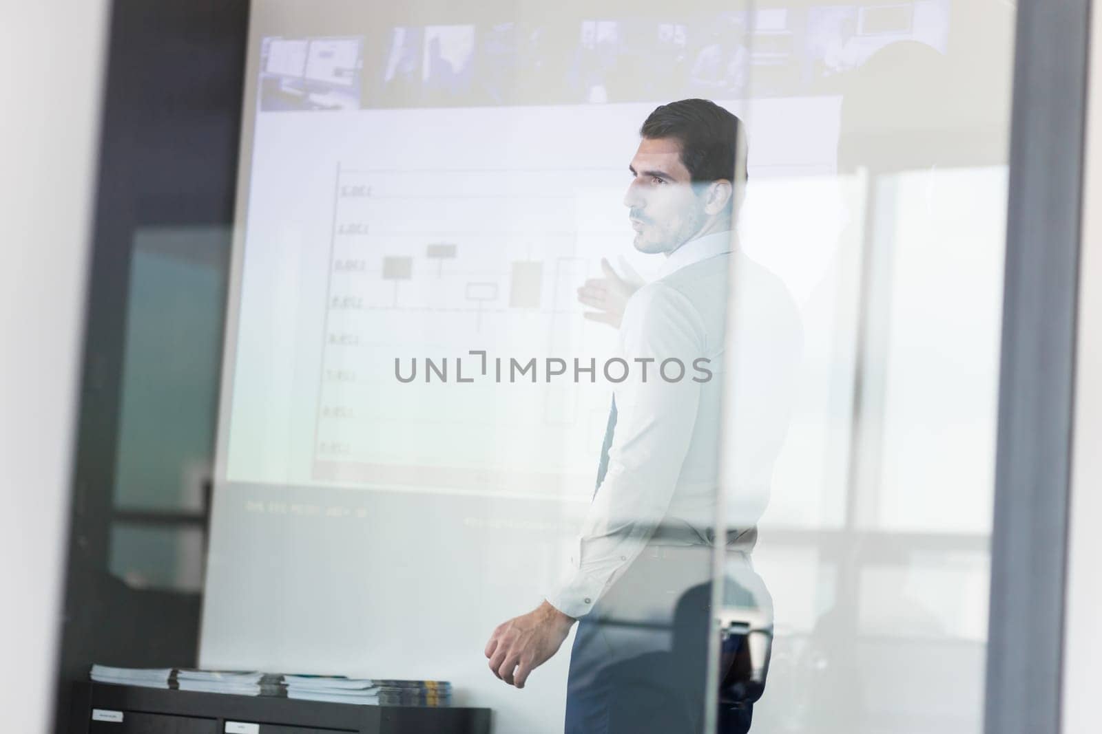 Business man making a presentation in front of whiteboard. View through glass.