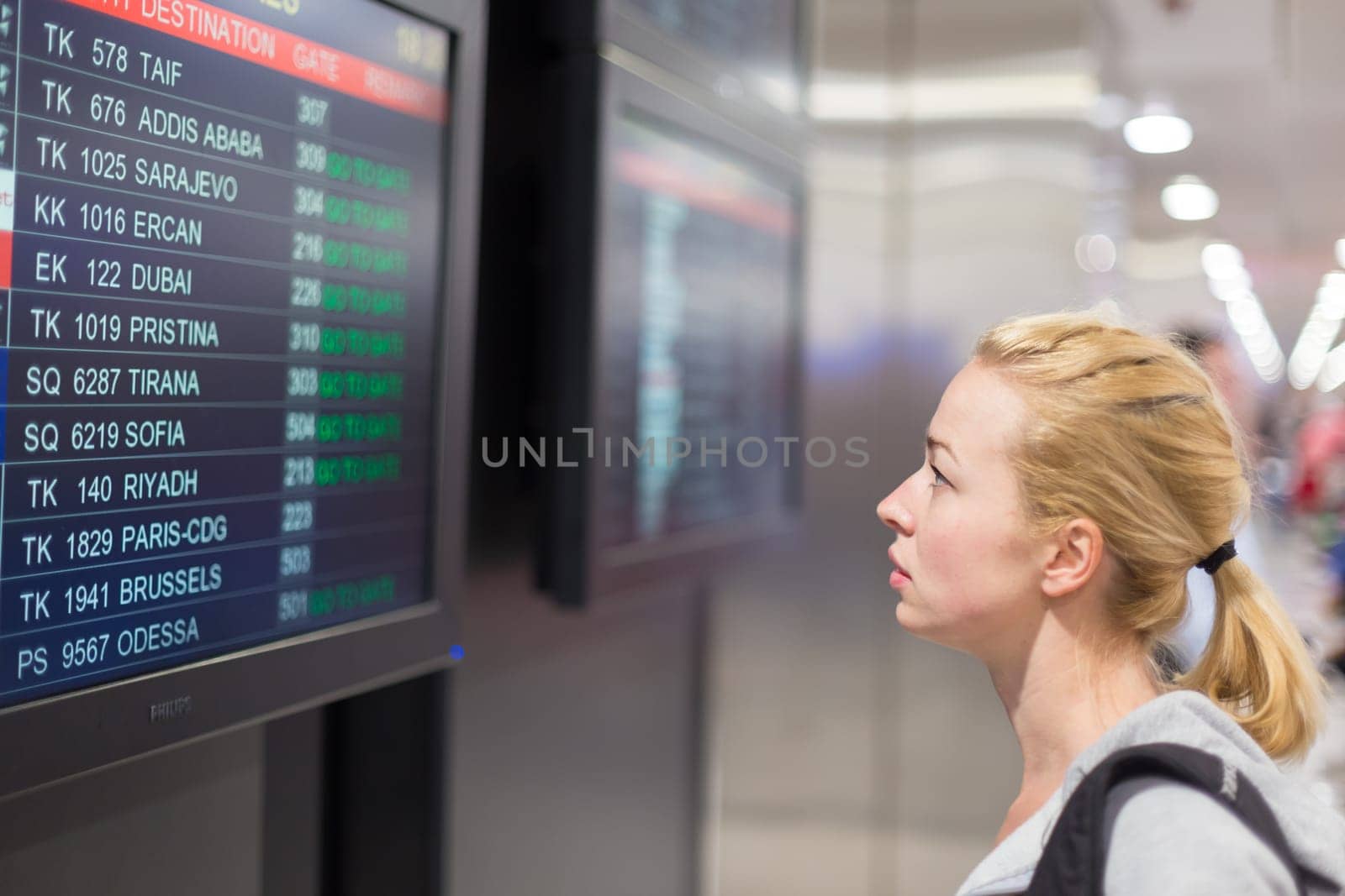 Young woman in international airport looking at the flight information board, checking her flight.