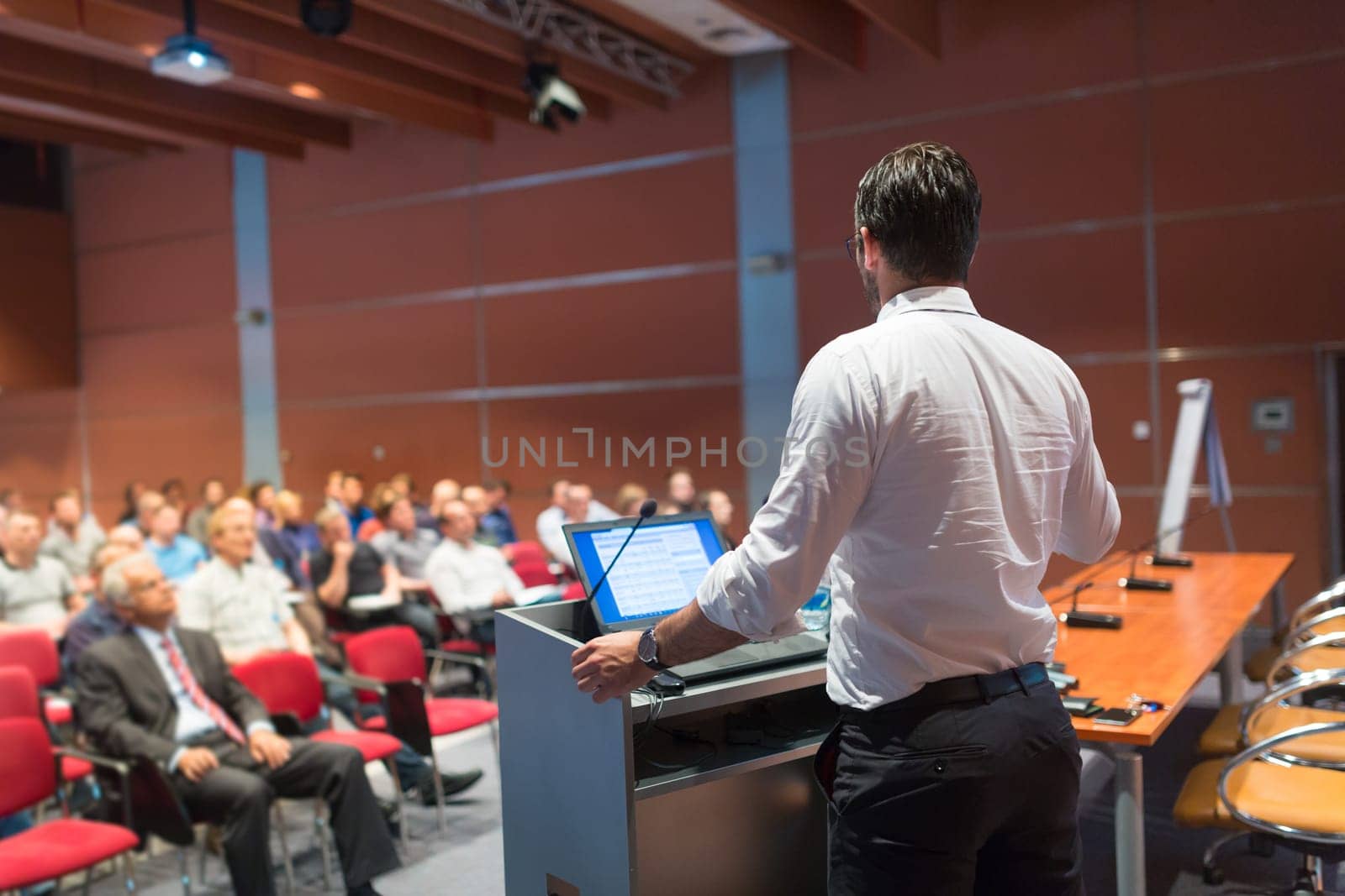 Speaker giving a talk on corporate Business Conference. Audience at the conference hall. Business and Entrepreneurship event.
