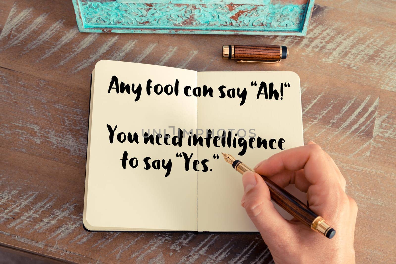 Retro effect and toned image of a woman hand writing on a notebook. Handwritten quote Any fool can say &quot Ah!&quot  You need intelligence to say &quot Yes&quot   as inspirational concept image