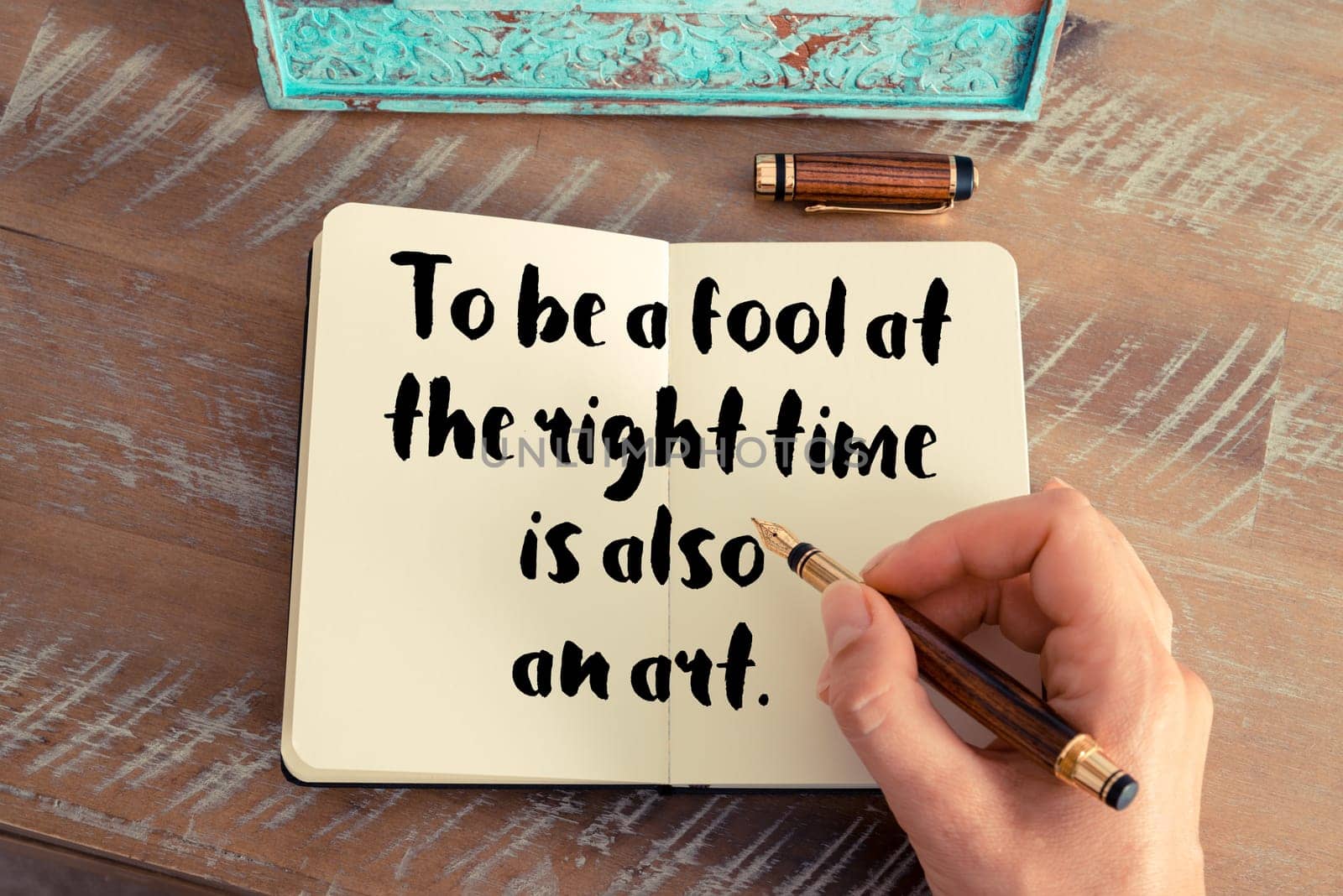 Retro effect and toned image of a woman hand writing on a notebook. Handwritten quote To be a fool at the right time is also an art as inspirational concept image