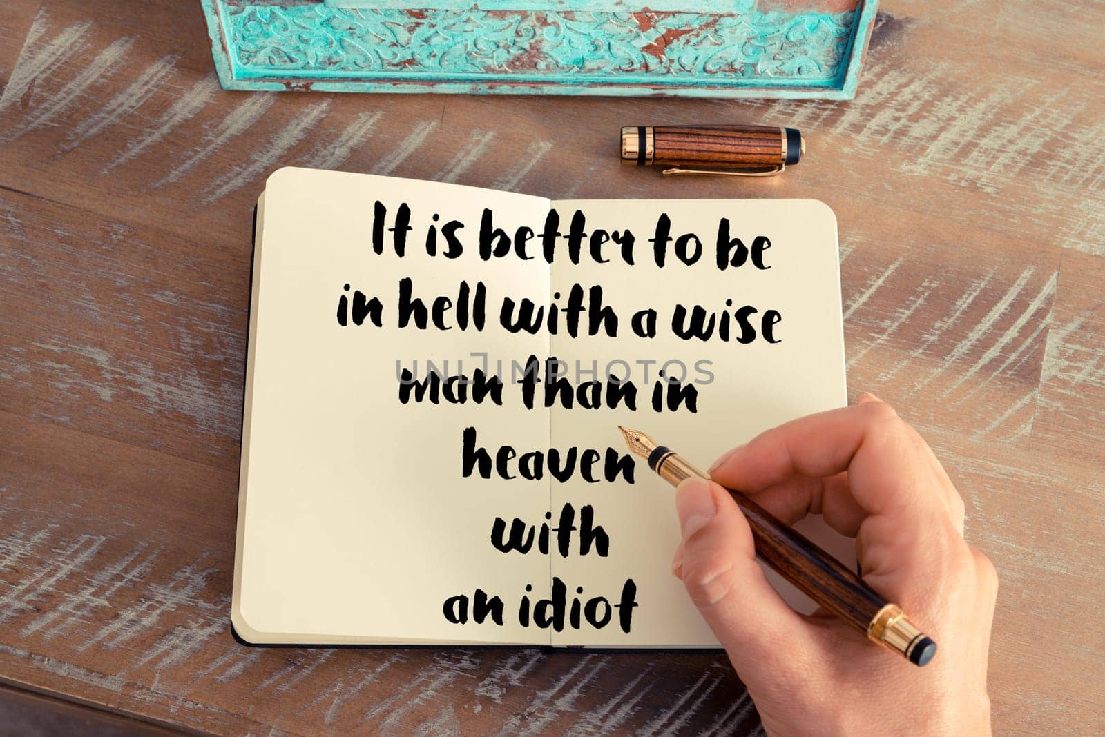 Retro effect and toned image of a woman hand writing on a notebook. Handwritten quote It is better to be in hell with a wise man than in heaven with an idiot as inspirational concept image