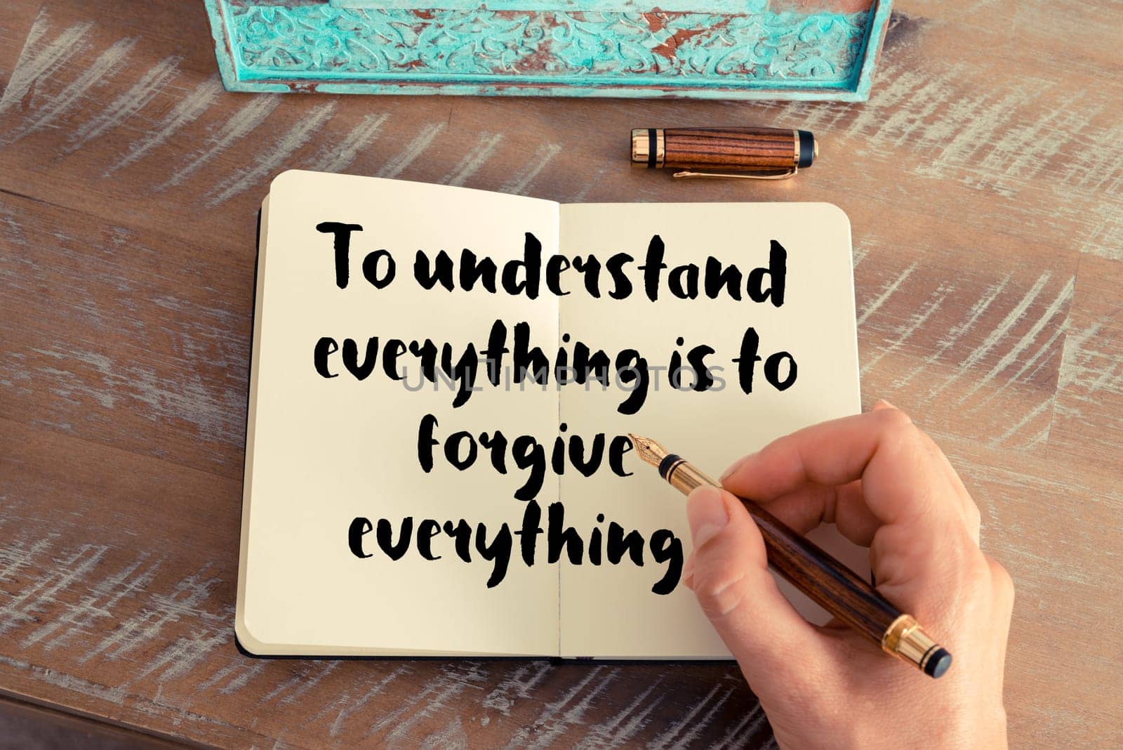 Retro effect and toned image of a woman hand writing on a notebook. Handwritten quote To understand everything is to forgive everything as inspirational concept image