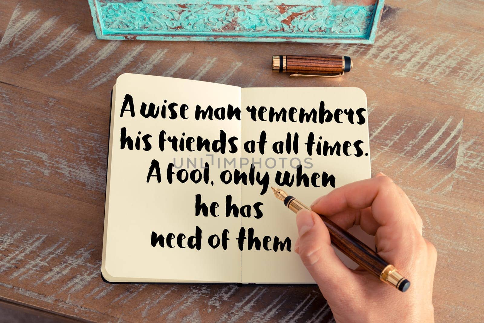 Retro effect and toned image of a woman hand writing on a notebook. Handwritten quote A wise man remembers his friends at all times  a fool, only when he has need of them as inspiration concept image