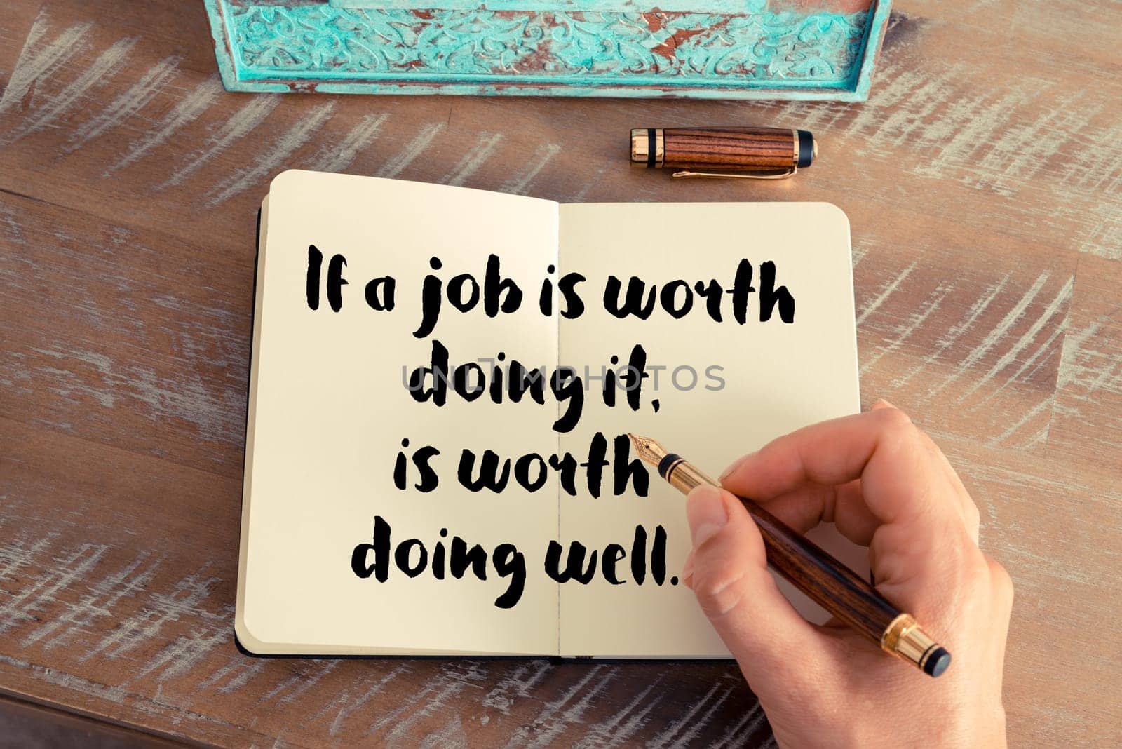 Retro effect and toned image of a woman hand writing on a notebook. Handwritten quote If a job is worth doing it is worth doing well as inspirational concept image
