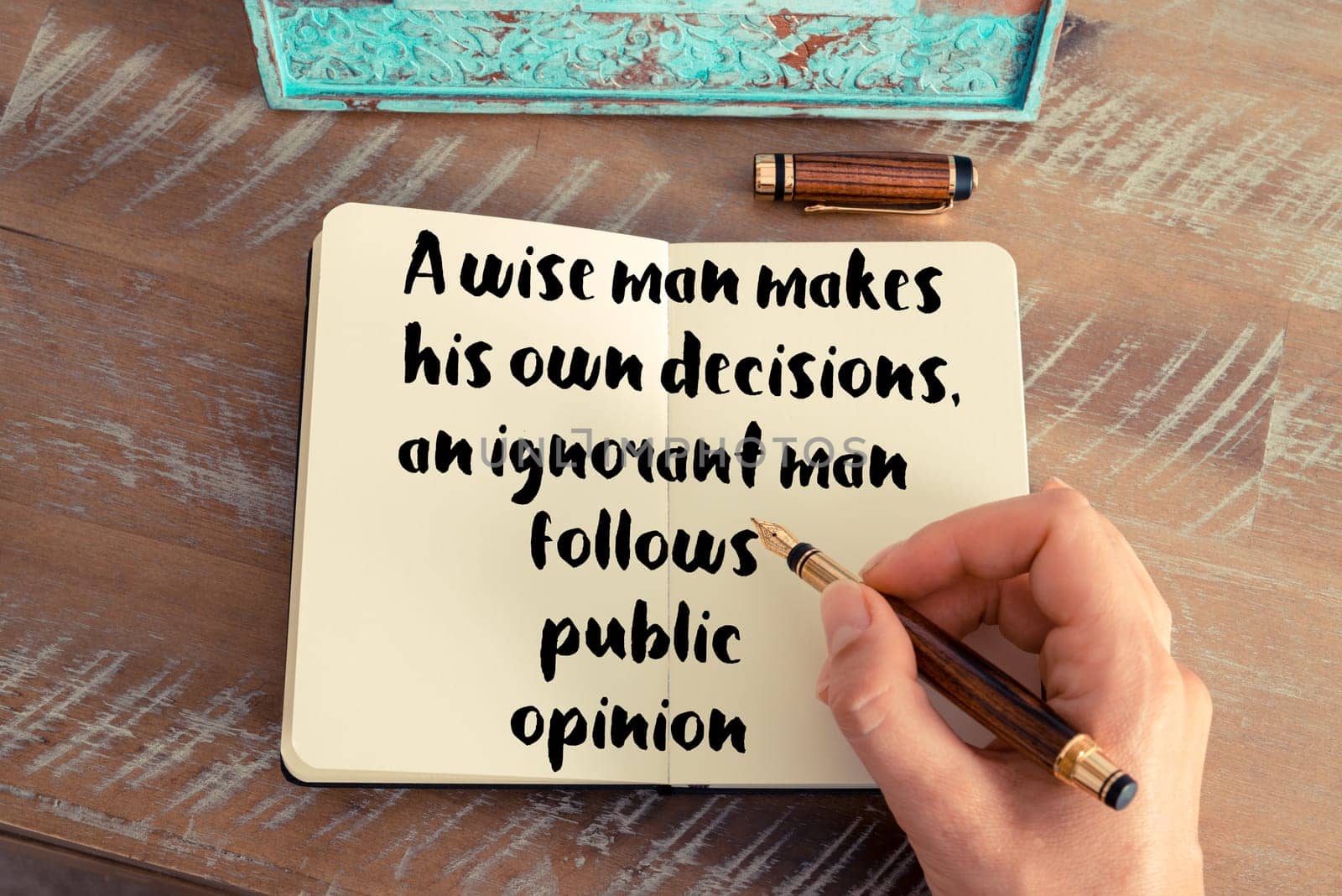 Retro effect and toned image of a woman hand writing on a notebook. Handwritten quote A wise man makes his own decisions, an ignorant man follows public opinion as inspirational concept image