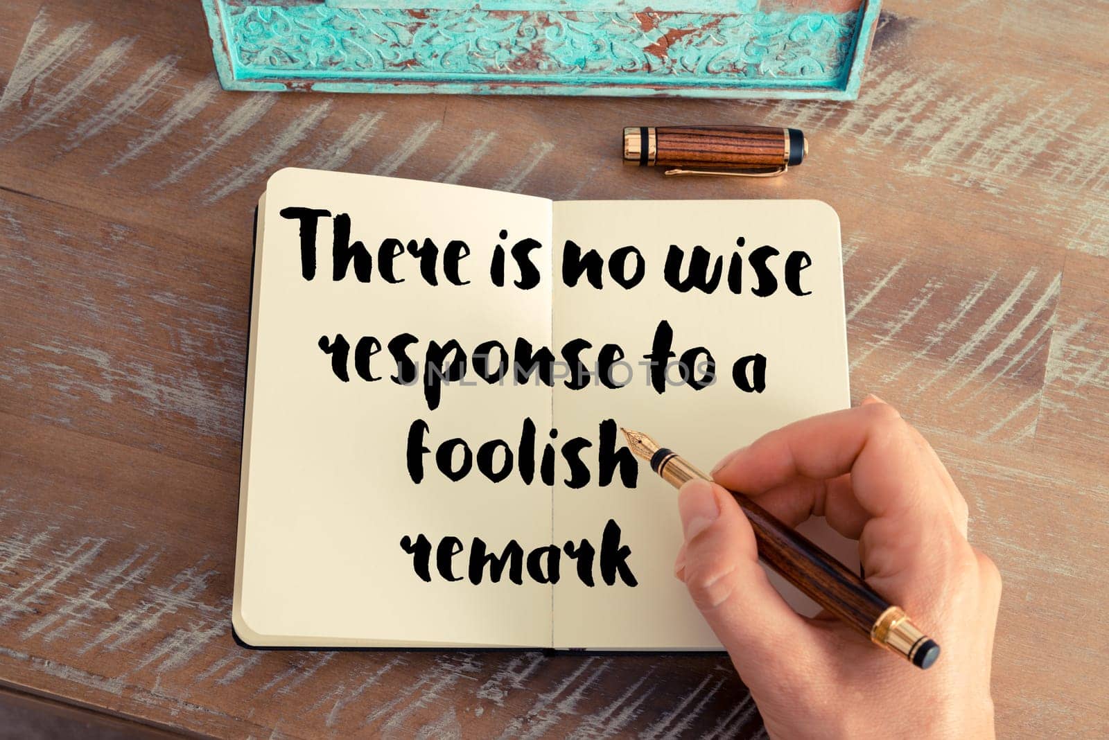 Retro effect and toned image of a woman hand writing on a notebook. Handwritten quote There is no wise response to a foolish remark as inspirational concept image