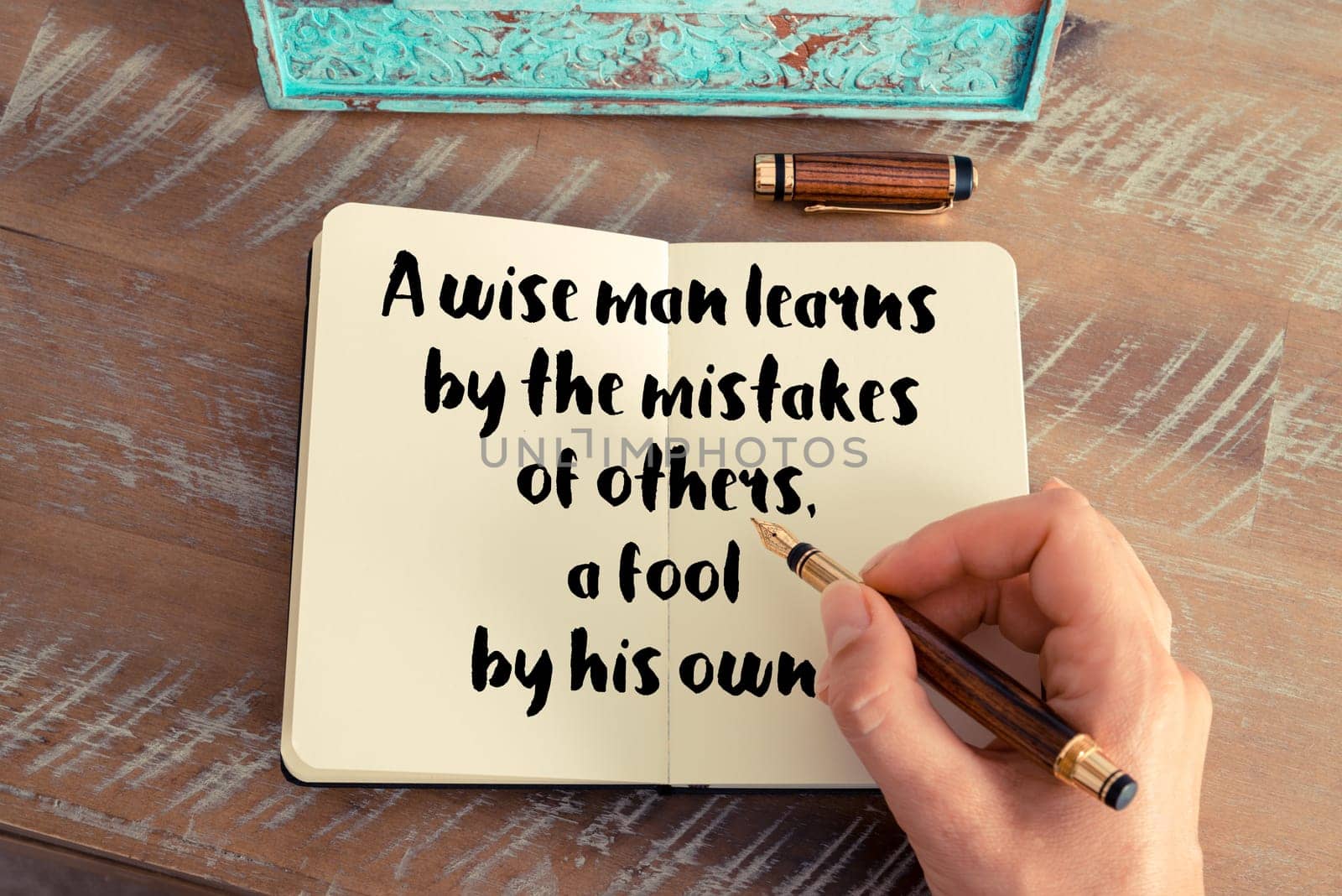 Retro effect and toned image of a woman hand writing on a notebook. Handwritten quote A wise man learns by the mistakes of others, a fool by his own as inspirational concept image