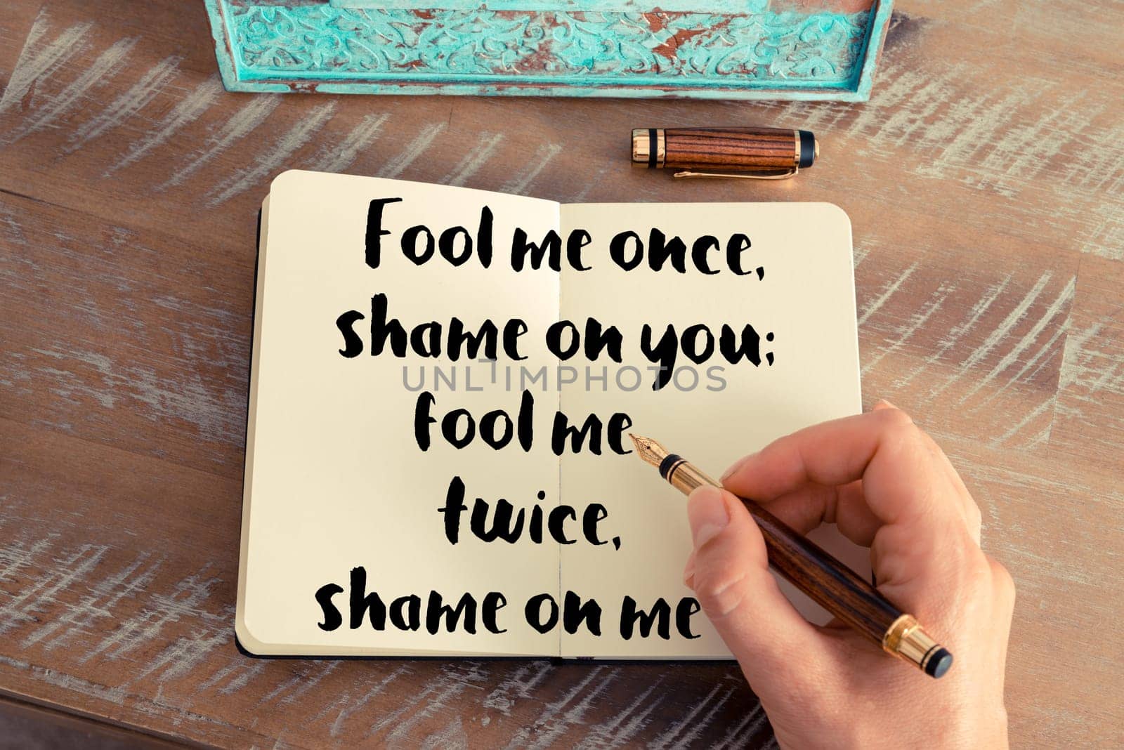 Retro effect and toned image of a woman hand writing on a notebook. Handwritten quote Fool me once, shame on you  fool me twice, shame on me as inspirational concept image