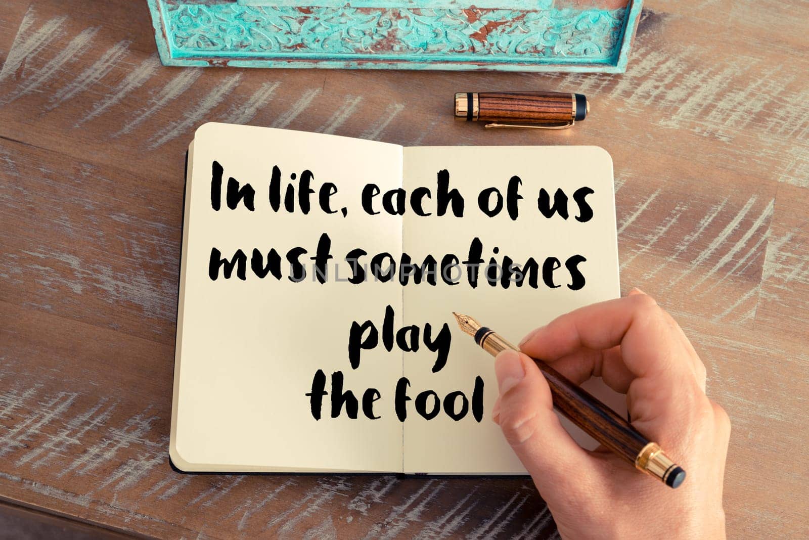 Retro effect and toned image of a woman hand writing on a notebook. Handwritten quote In life, each of us must sometimes play the fool as inspirational concept image