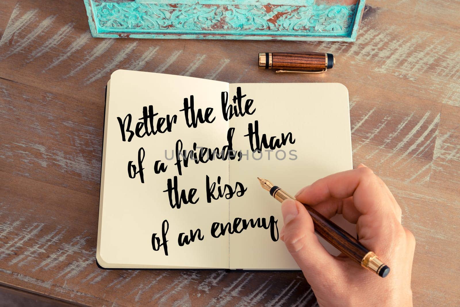 Retro effect and toned image of a woman hand writing on a notebook. Handwritten quote Better the bite of a friend, than the kiss of an enemy as inspirational concept image